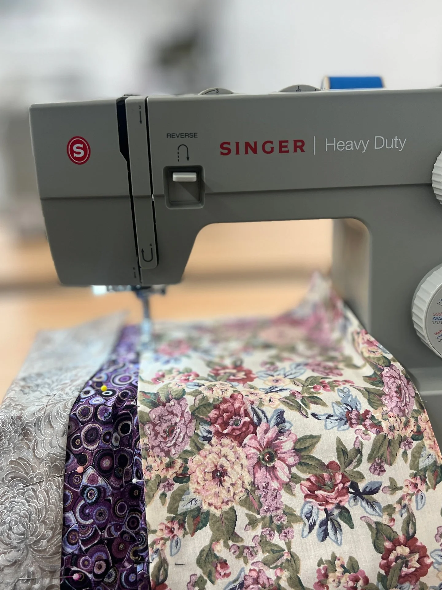 Close-up of sewing machine stitching floral and patterned fabric.