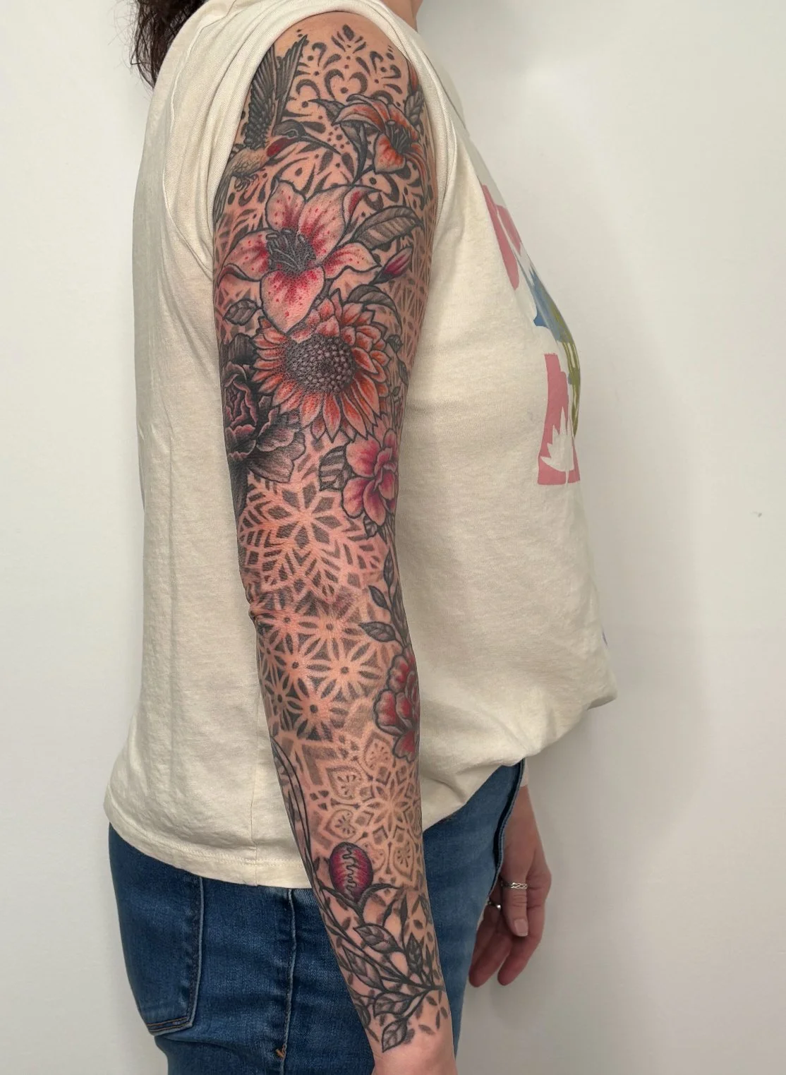 A person with a full sleeve tattoo featuring flowers, leaves, and geometric patterns on their arm. State Of The Art Tattooing Winchester Virginia 