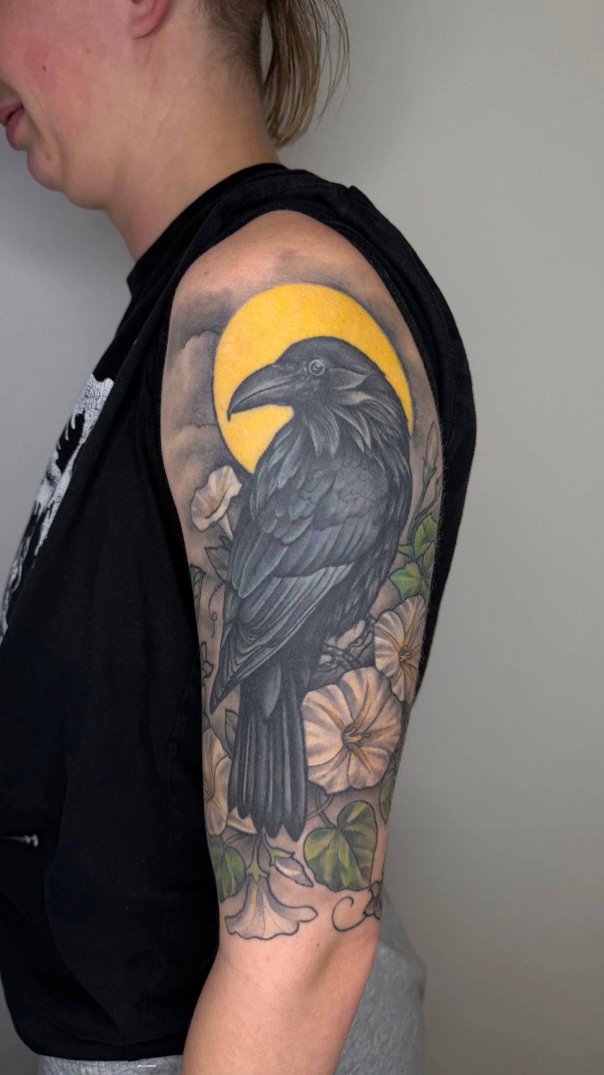 Tattoo of a black crow with a yellow moon or sun behind it, with flowers and leaves around. Done in Winchester Virginia by Jordan Joyes 