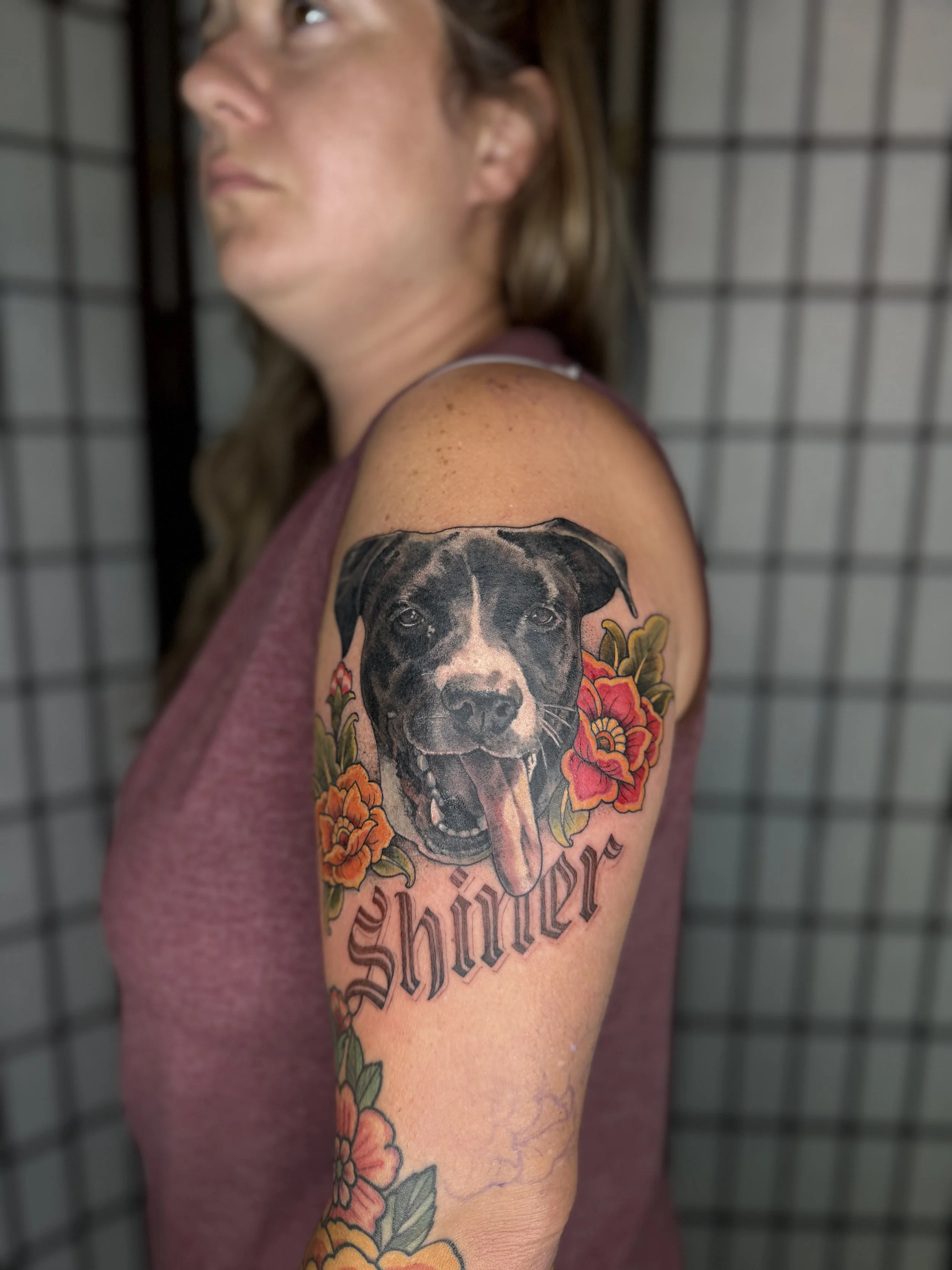 A woman with a tattoo of a fierce black dog surrounded by colorful flowers on her upper arm. Done by Jordan Joyes in Kyle Texas