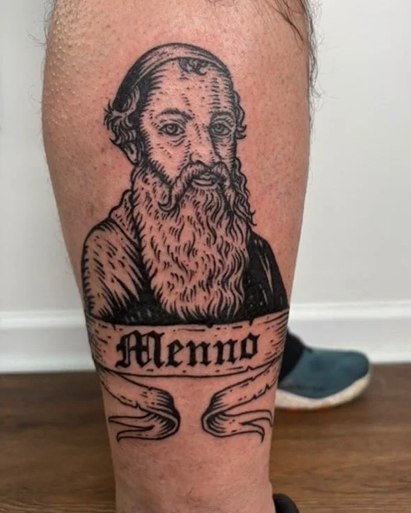 Tattoo of a bearded man with long hair, labeled 'Meno,' on a person's leg. Custom Neil Stavely Tattoo State Of The Art Tattooing Winchester Virginia 