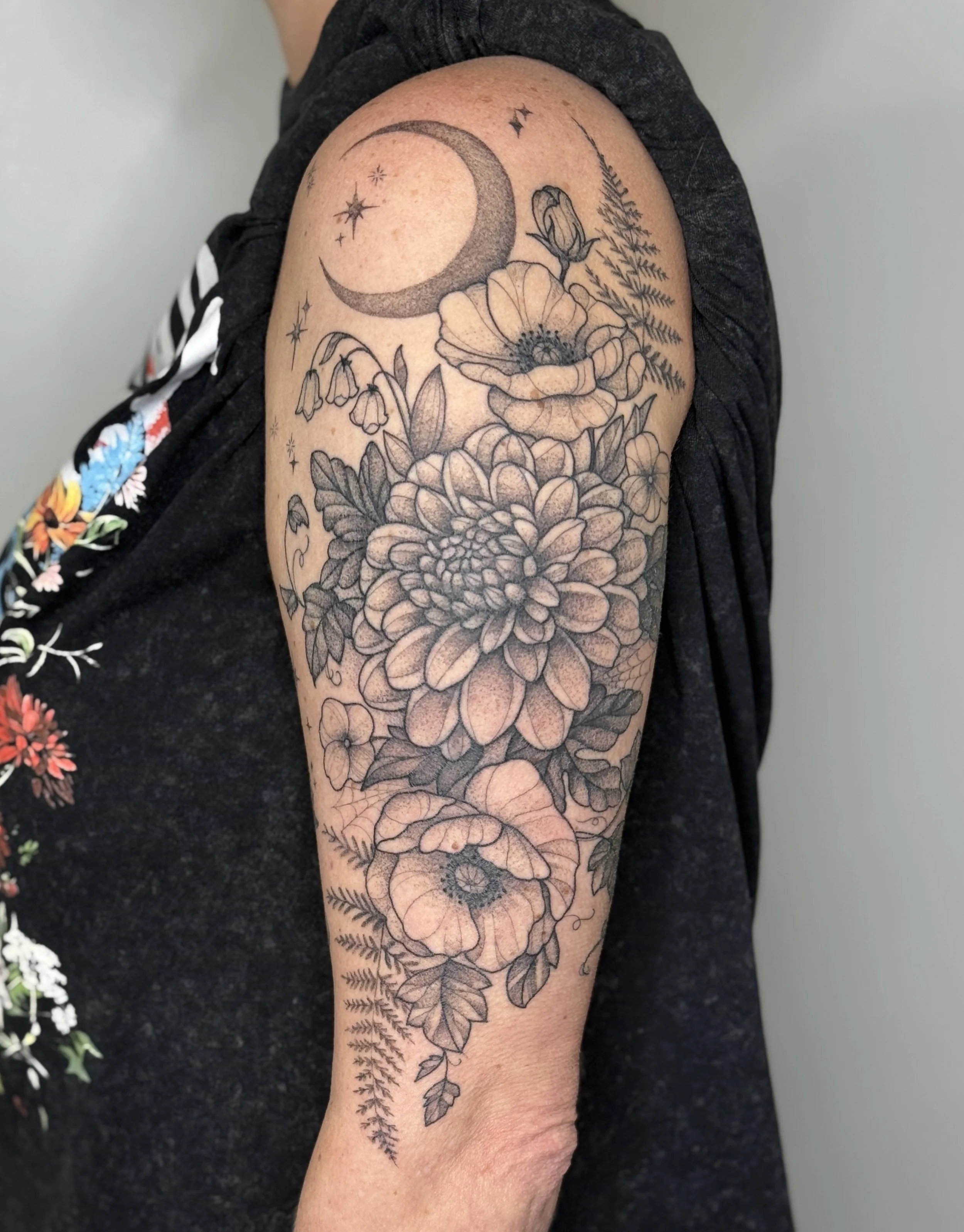 Black and gray floral tattoo by Jordan Joyes featuring a large chrysanthemum, ferns, and blooming flowers on the person's upper arm and shoulder.