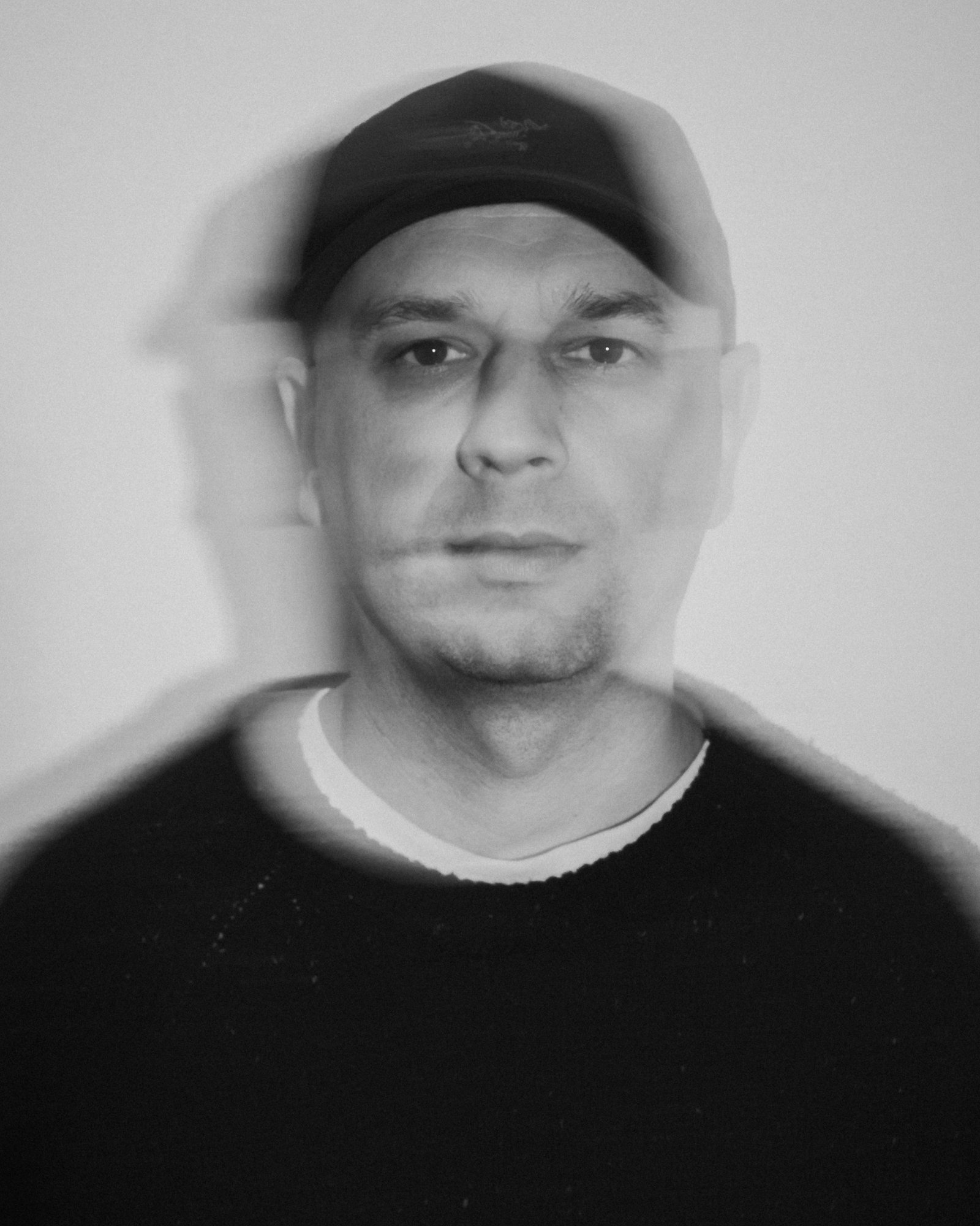 Black and white portrait of a man wearing a cap, with a blurred, layered effect.