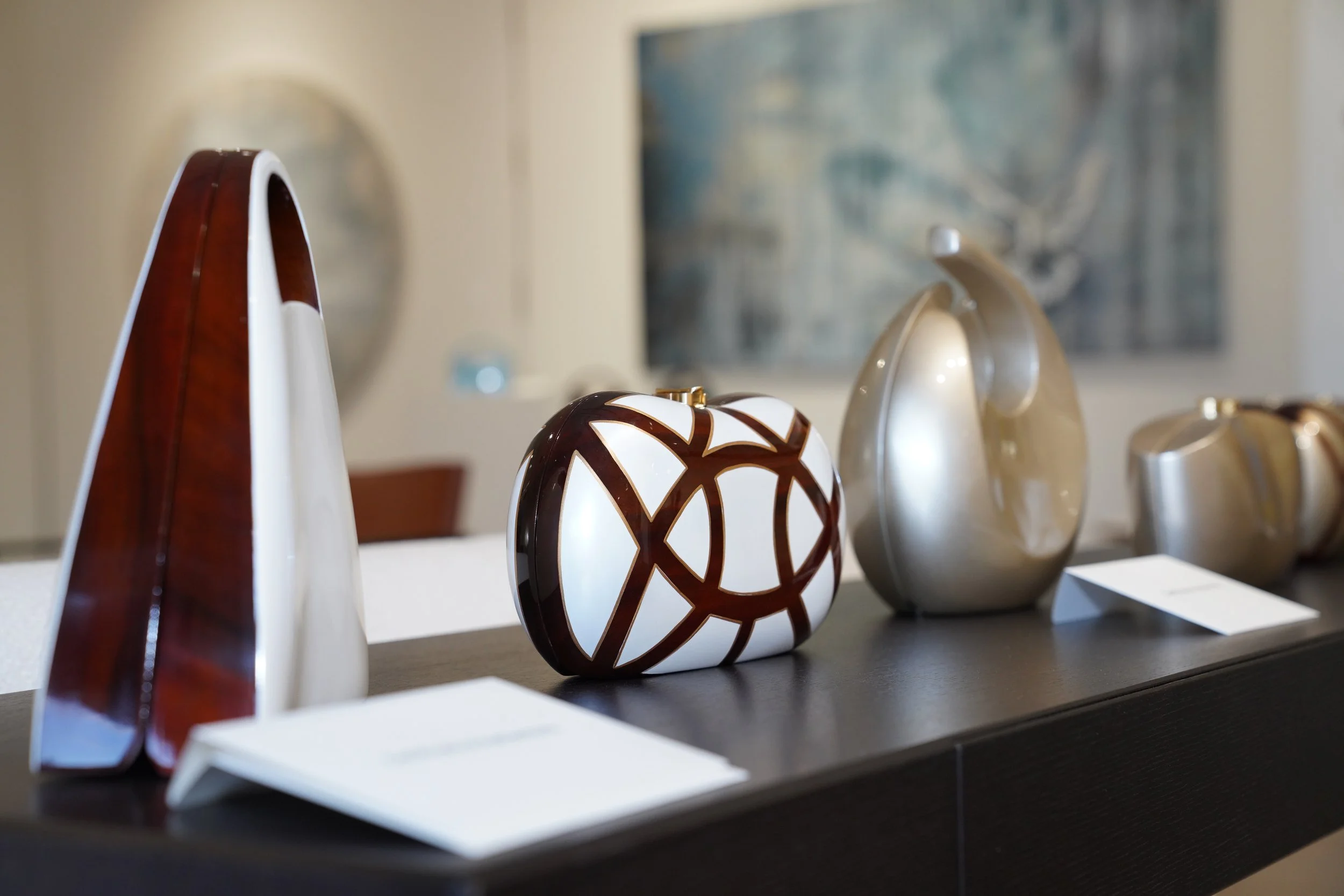 Display of decorative vases and sculptures on a dark table at an art gallery or exhibition.