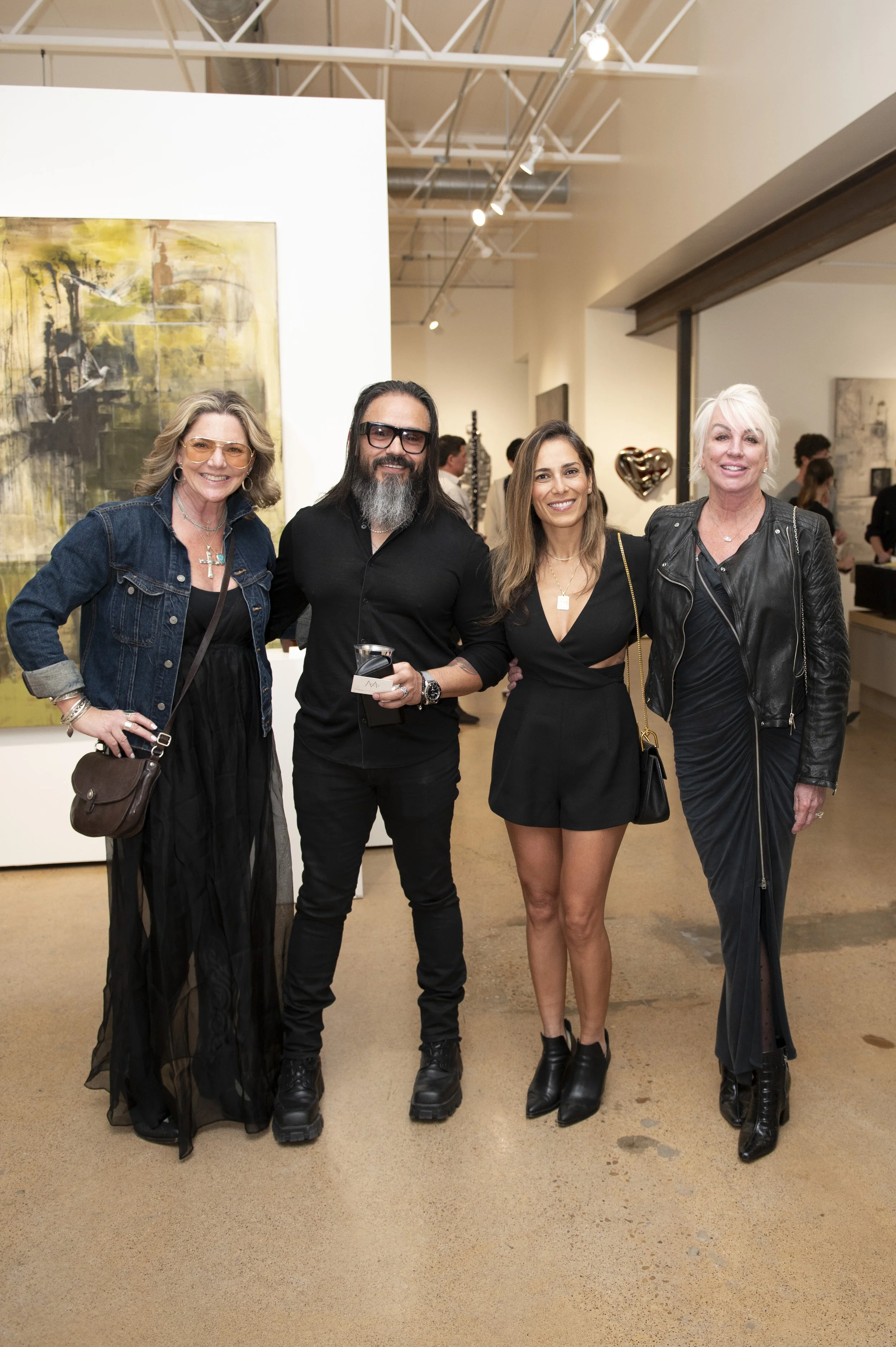 Four women and one man standing together at an art gallery, smiling and posing for a photo.