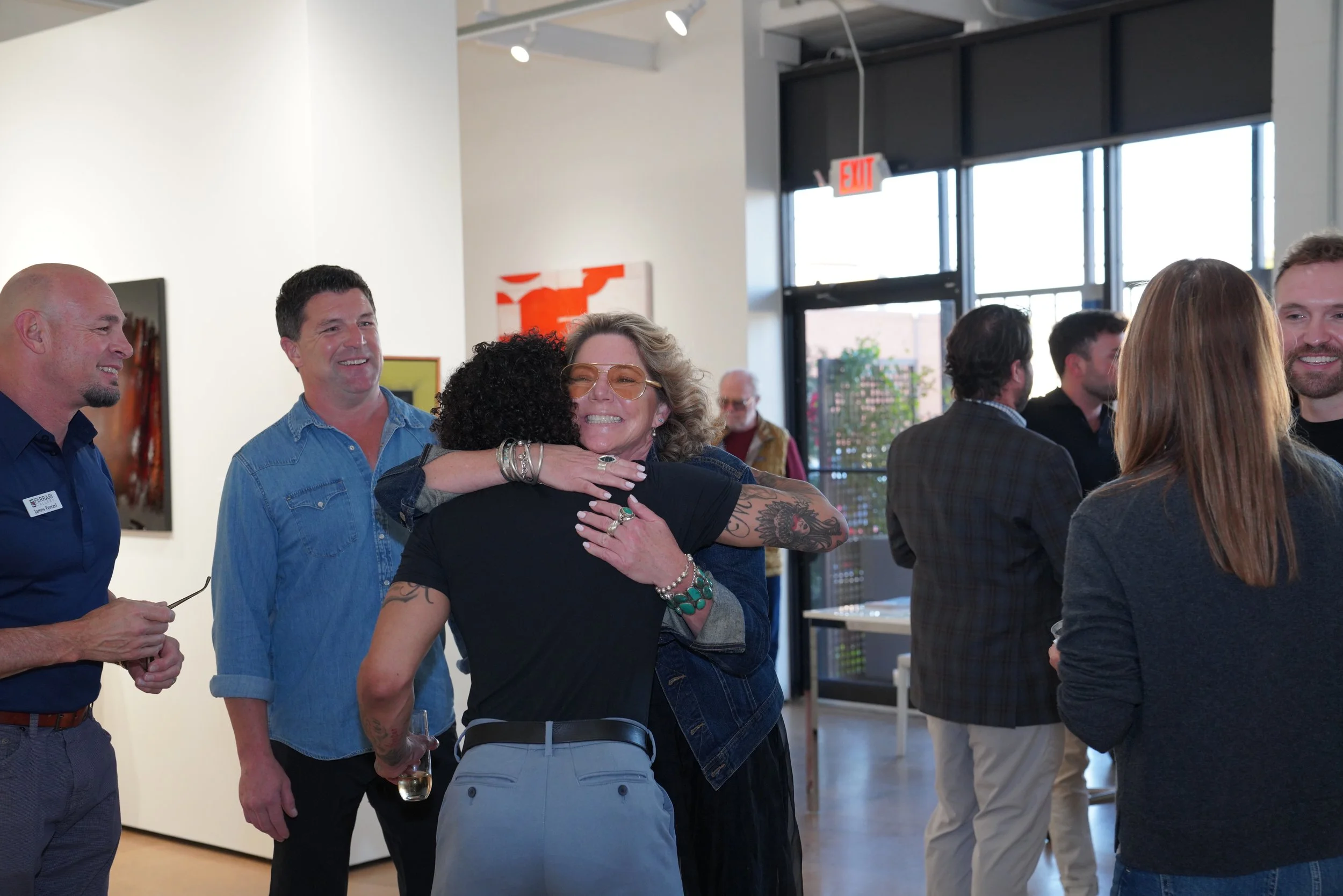 People gathering at an art gallery, smiling and hugging.