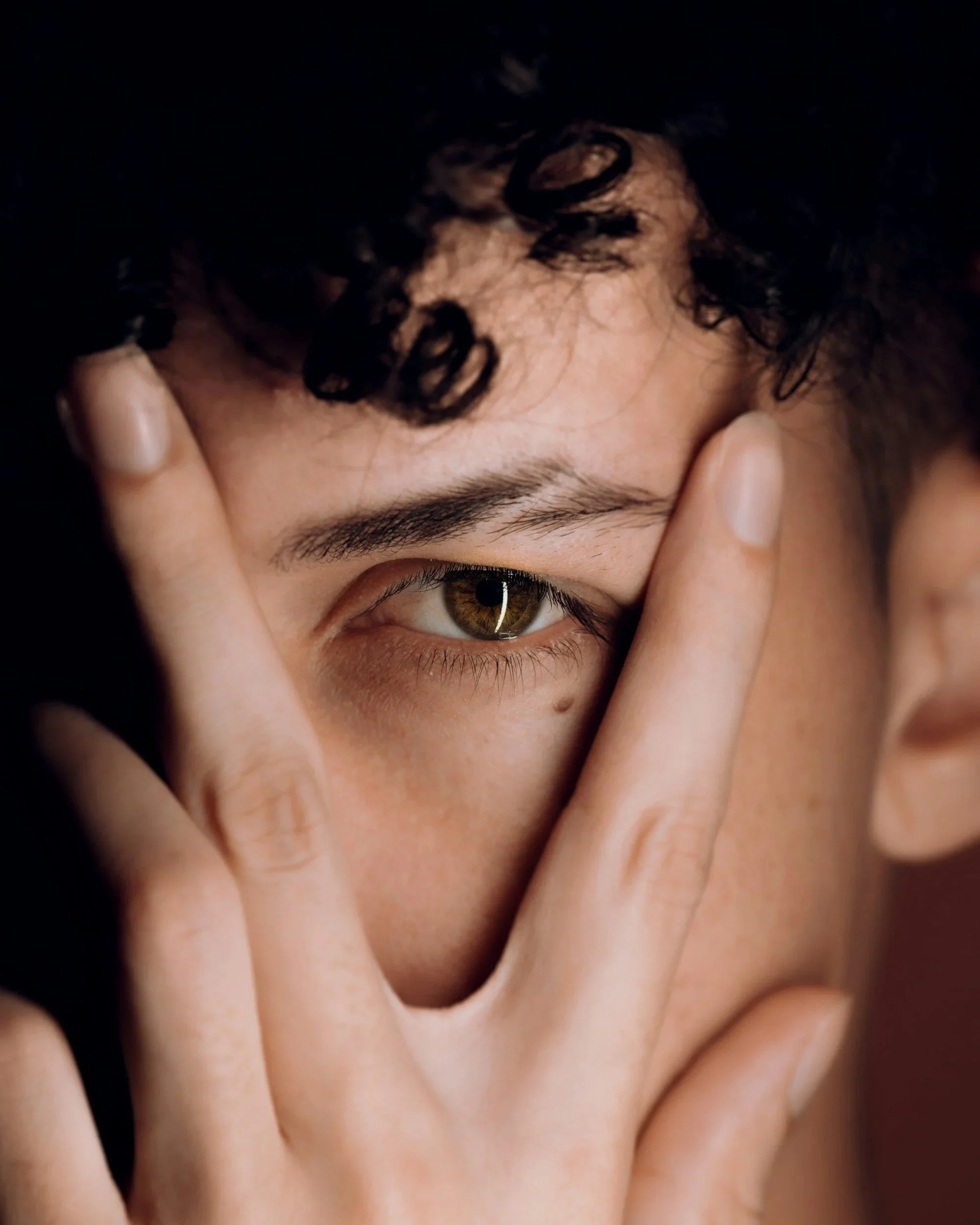 One eye of a man staring directly at the camera with his fingers in a V shape around his eye