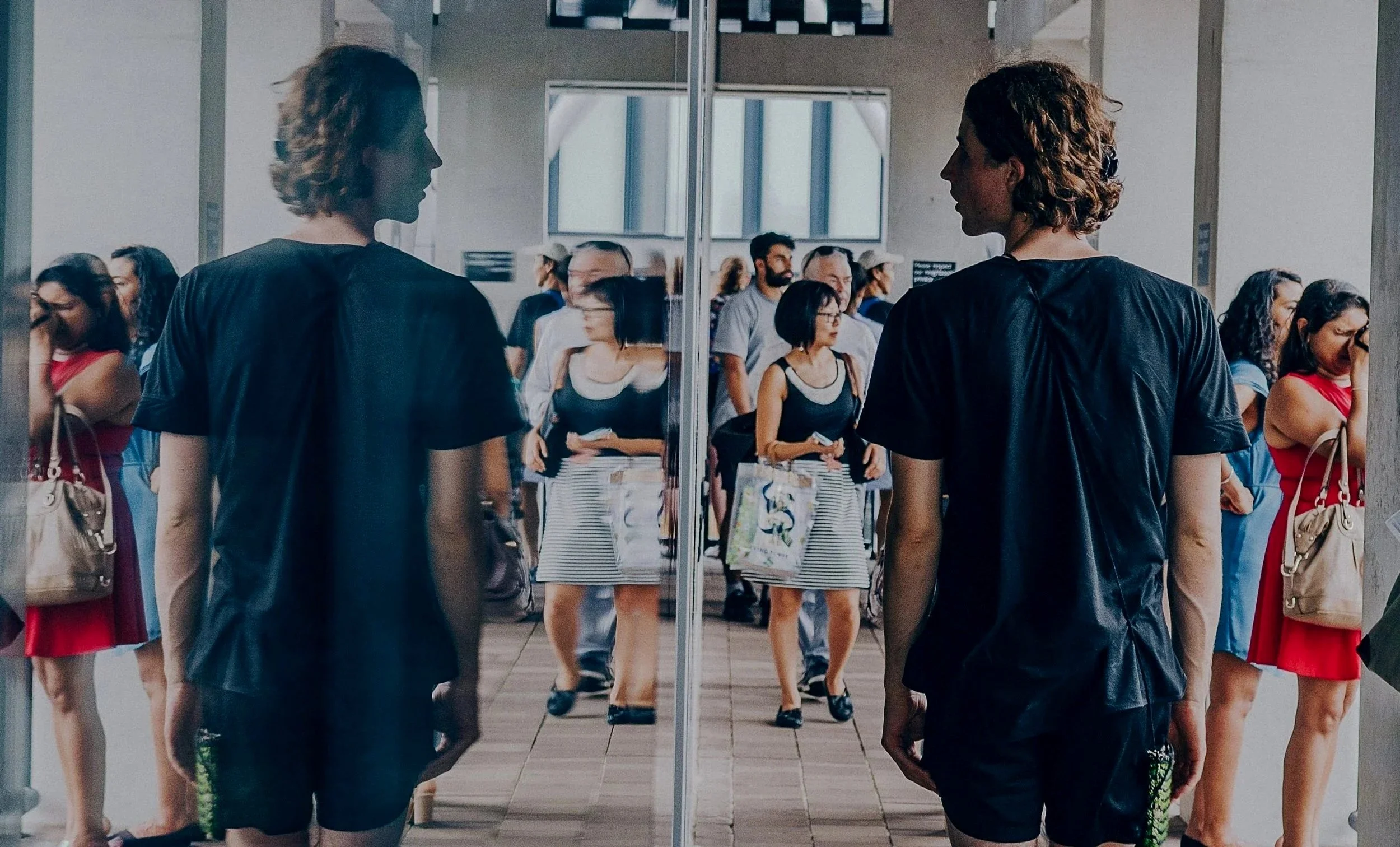A man walking past a wall coverd with a mirror and turning his head to see his reflection