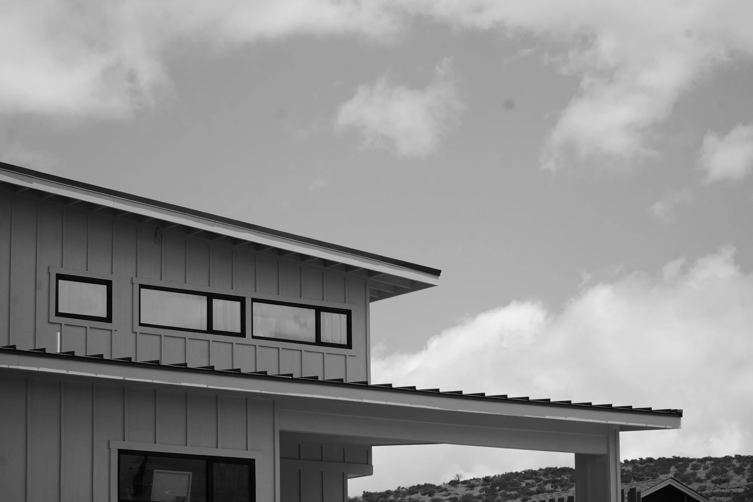 A close-up view of the corner of a modern house with large windows and horizontal siding, under a cloudy sky.