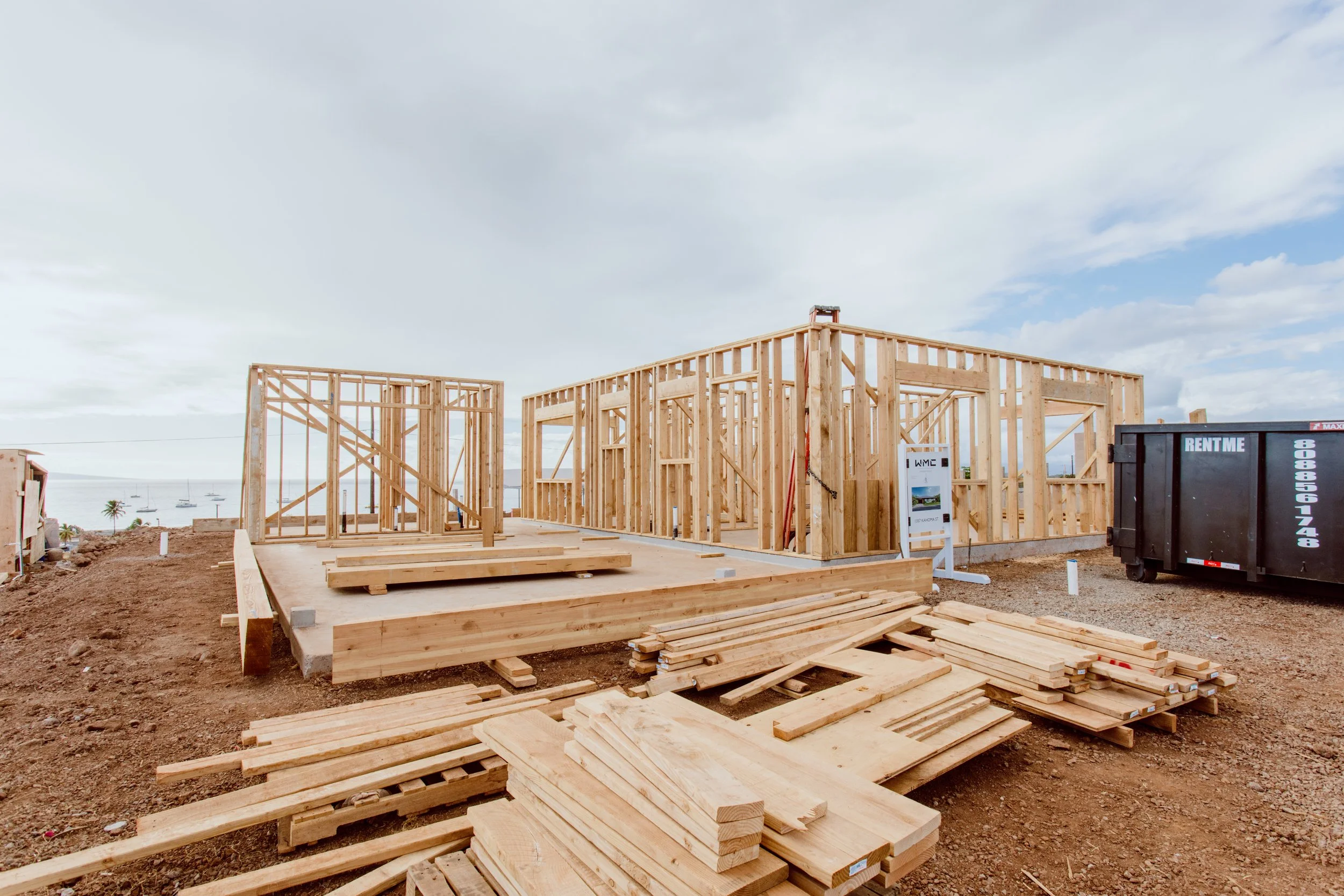 Wooden frame of a building under construction at a construction site overlooking the water with boats.