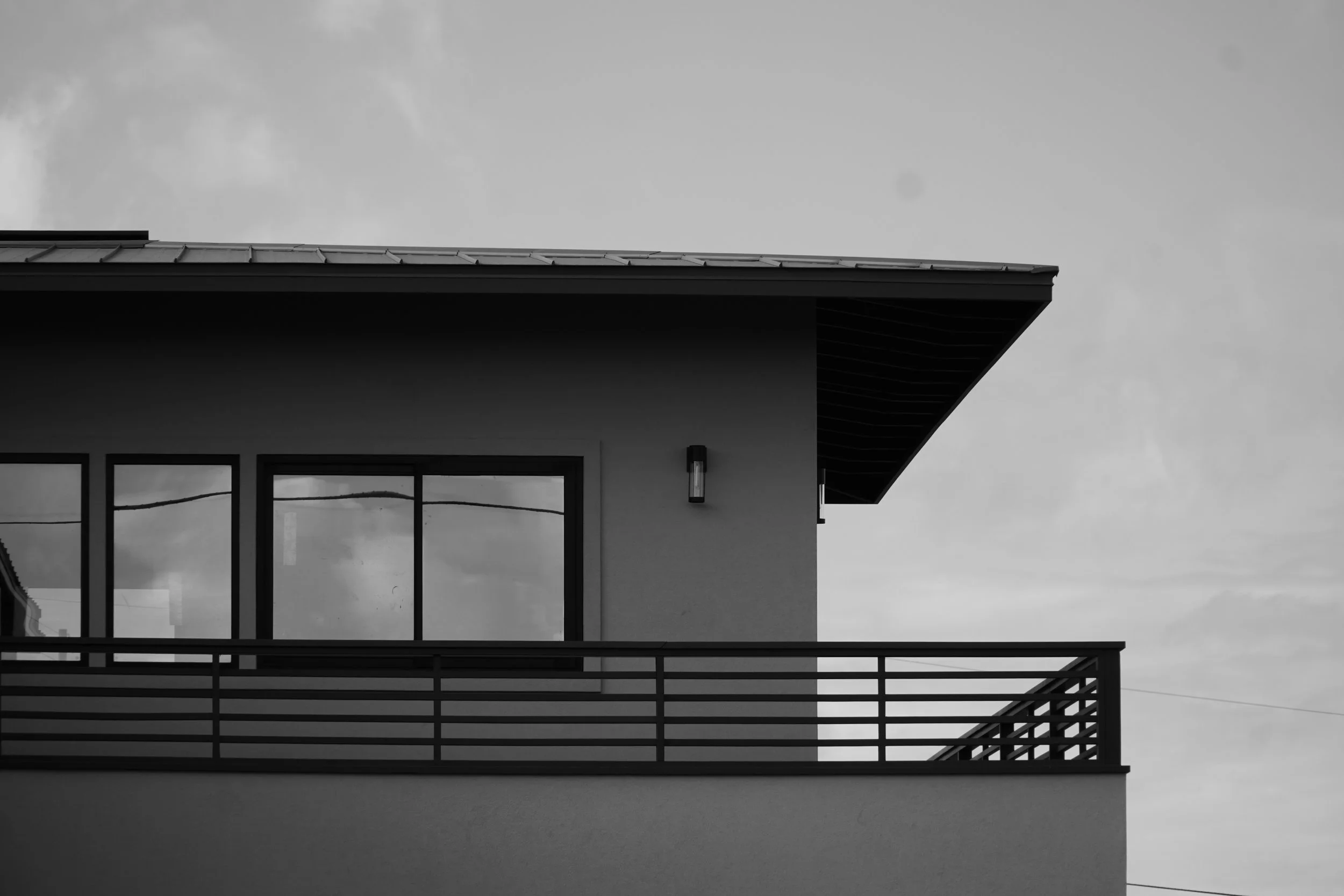 A black-and-white photo of a modern house with large windows and a balcony, under a cloudy sky.