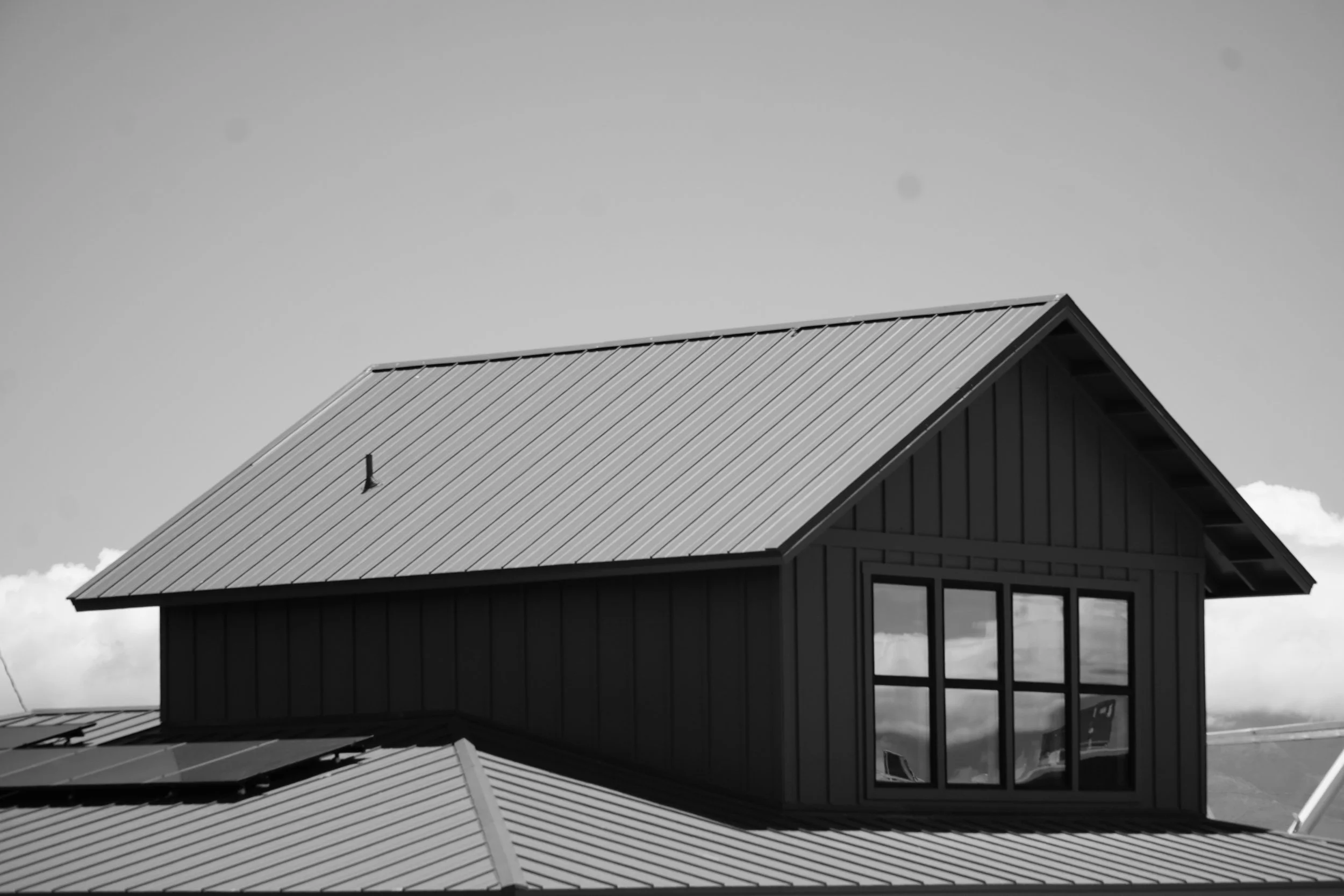 Black and white photo of a modern house with angled rooflines and large windows, set against a cloudy sky.