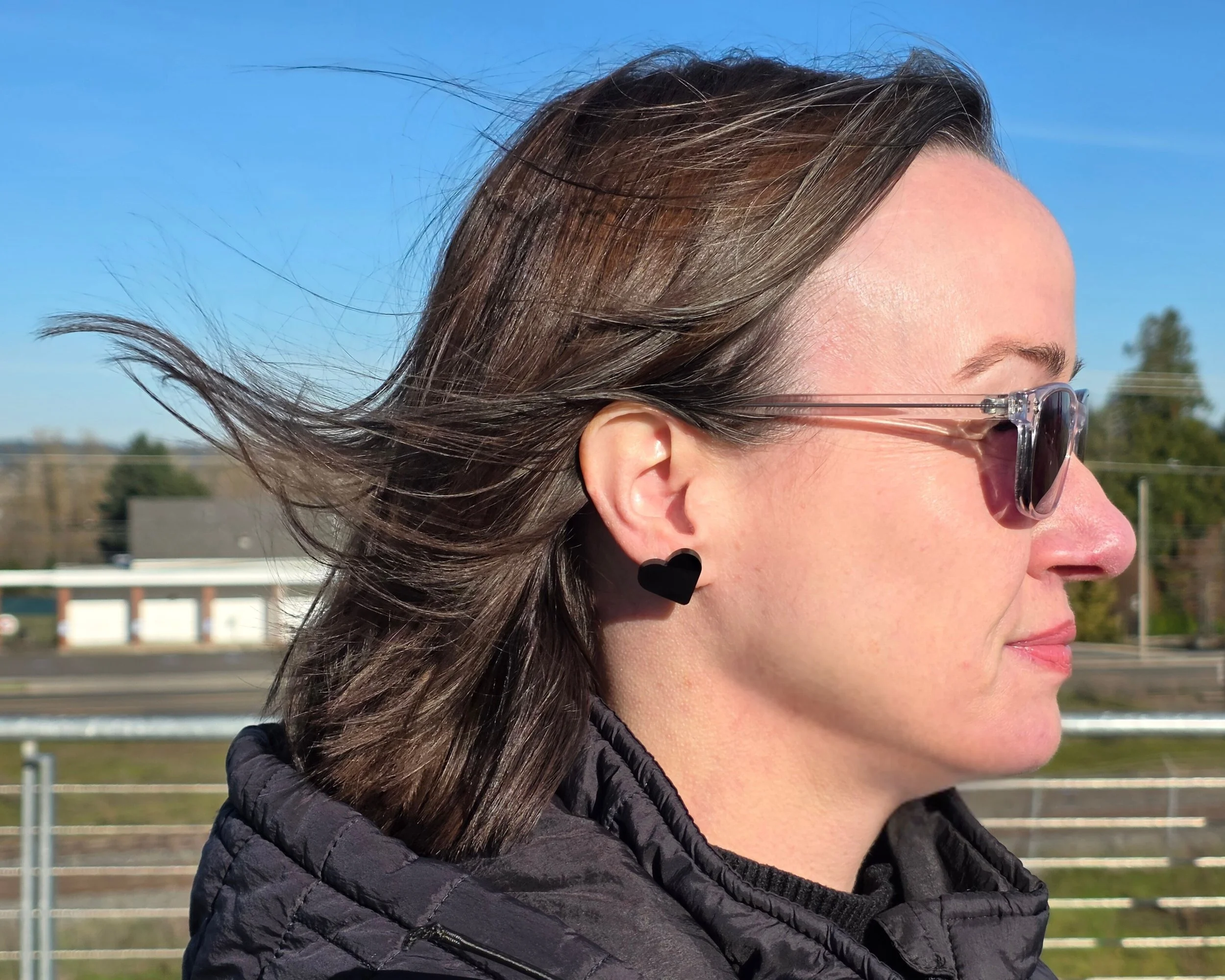 Black acrylic heart stud earring shown on ear in outdoor profile view, hypoallergenic titanium post stud earrings handmade by Rainbow Charlie