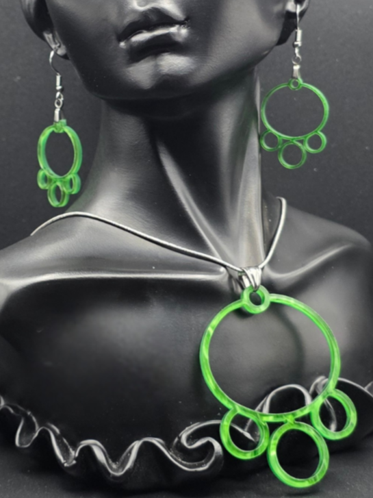 Custom earring and necklace set with translucent green circular shapes, the pendant built from linked open rings, shown on a dark display bust.