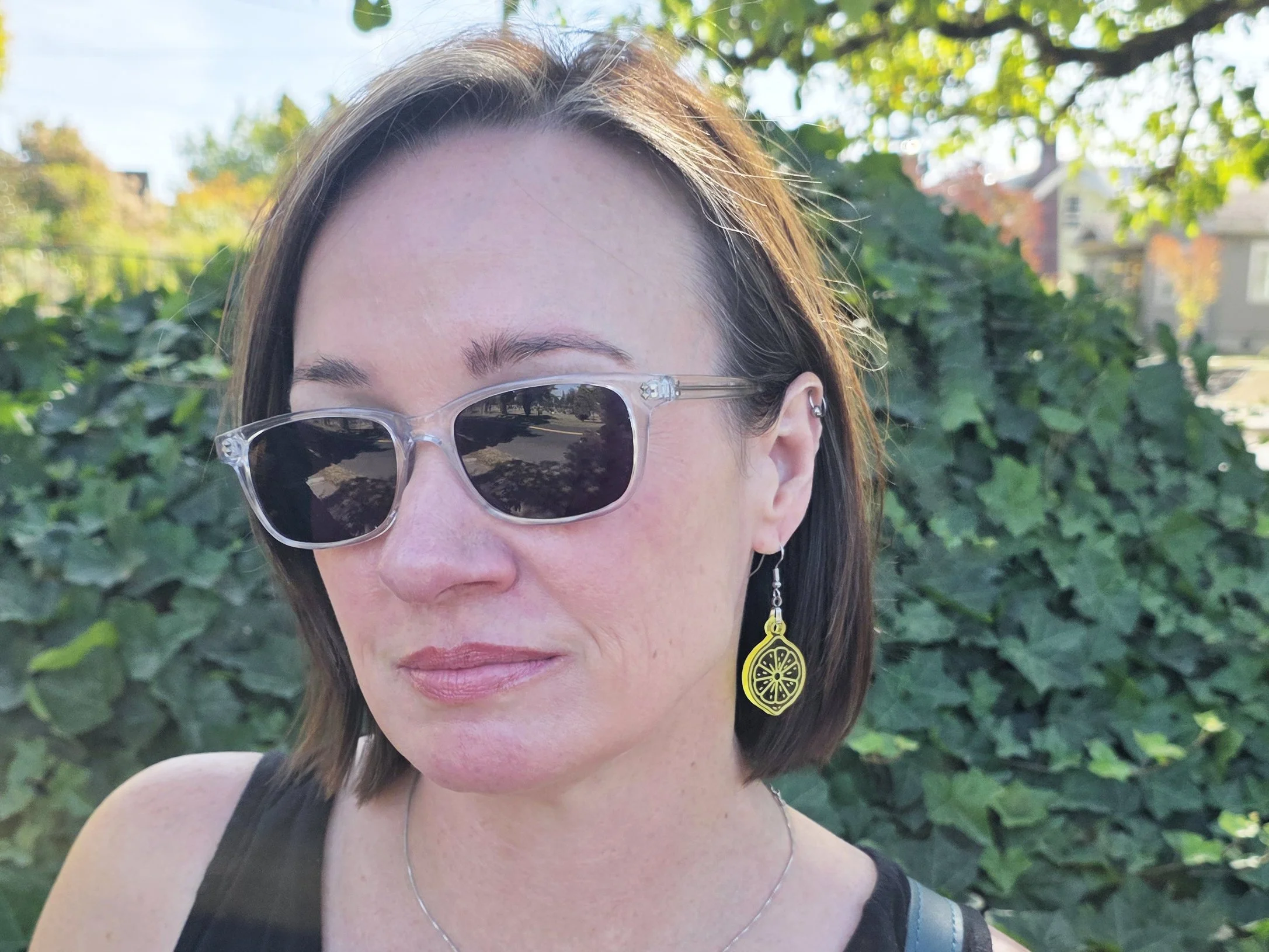 Yellow acrylic lemon slice earring worn by a model outdoors, close-up profile view with greenery in the background.