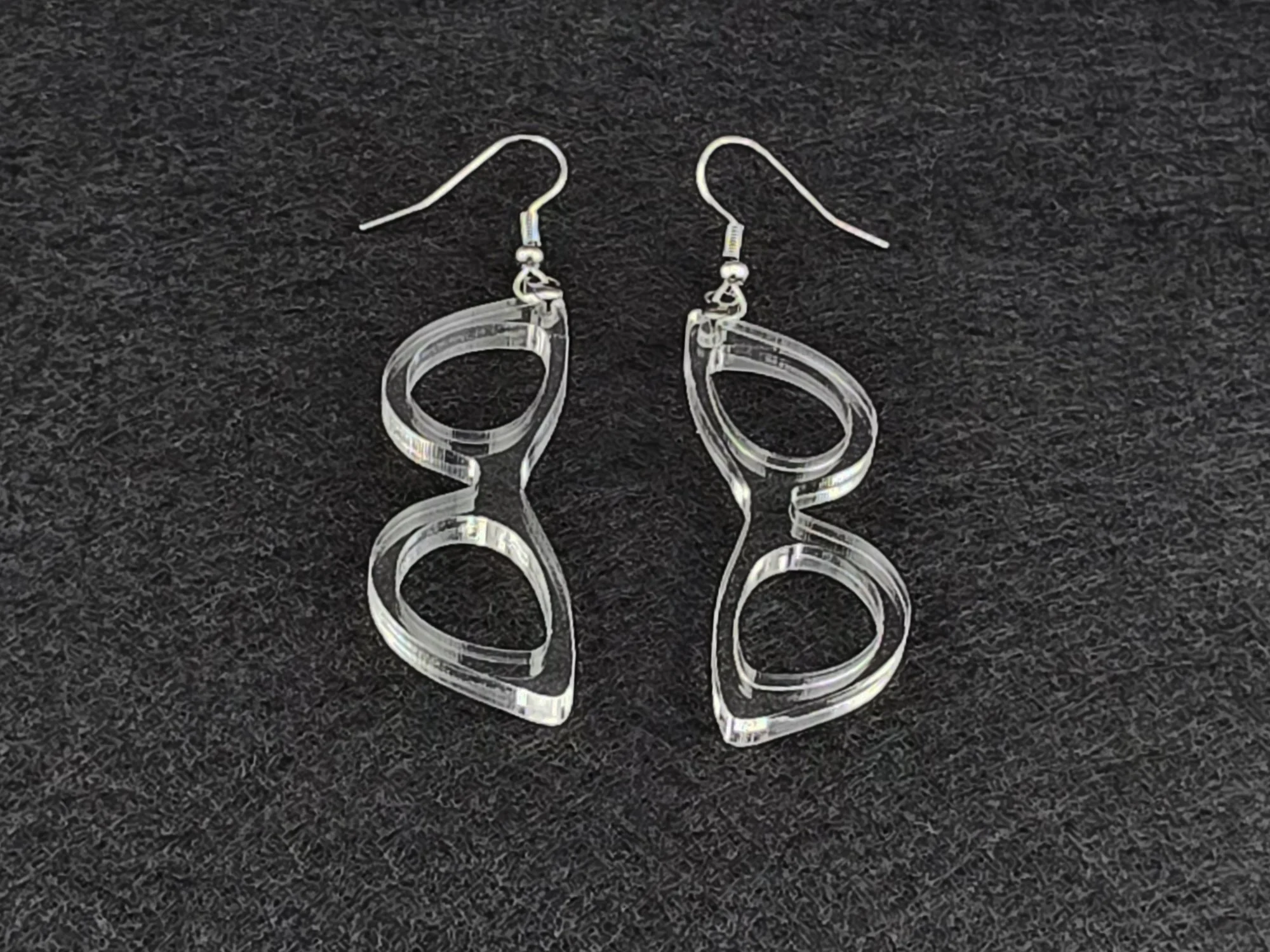Clear acrylic cat-eye earrings shown at an angle on a charcoal background, highlighting the cut linework with no color tint.
