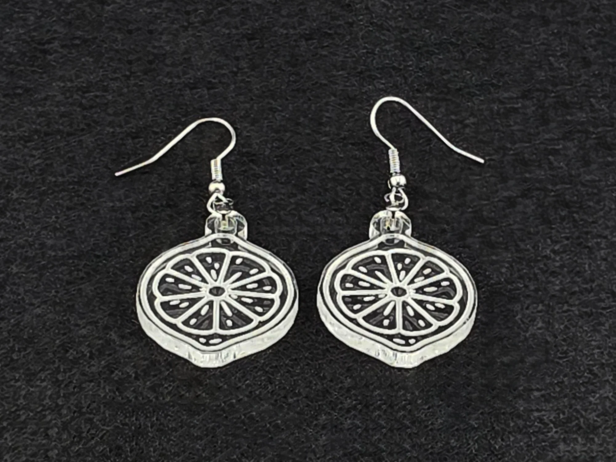 Clear acrylic lemon slice earrings shown at an angle, highlighting the engraved citrus detail and cut edge.