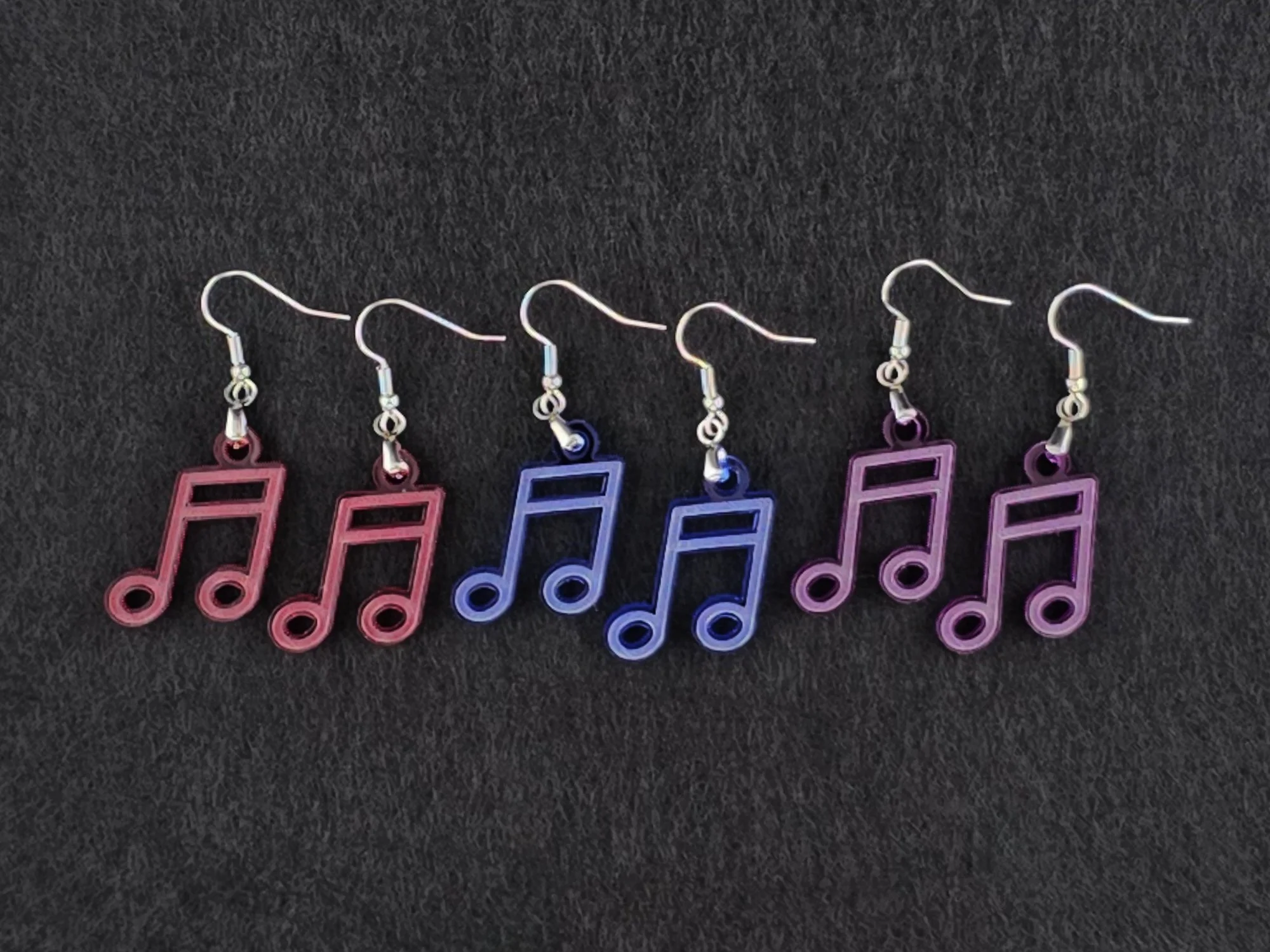 Three pairs of beam note earrings on charcoal in red, blue, and purple acrylic, shown side by side for color comparison.