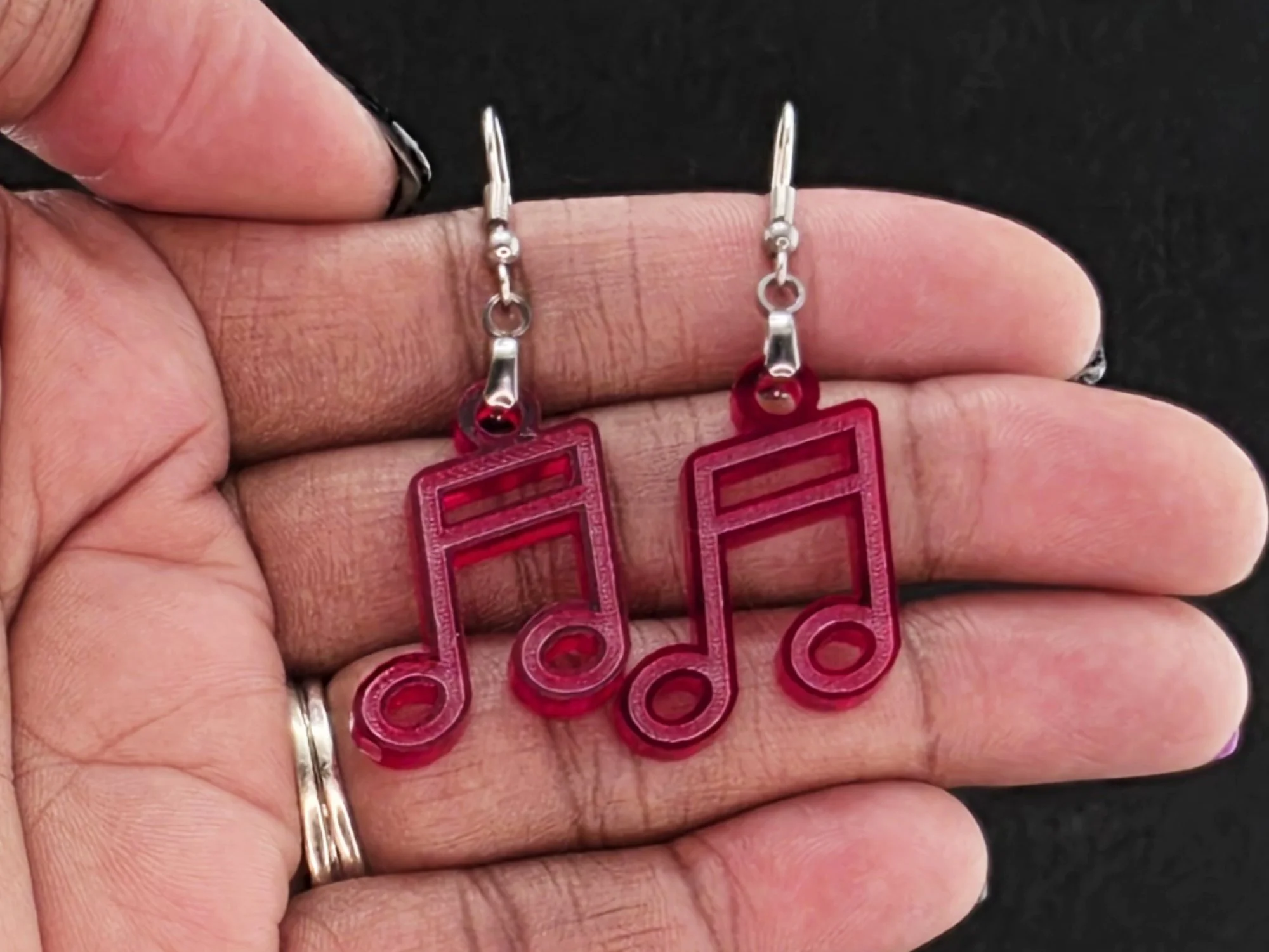 Beam note earrings in a red acrylic resting in an open palm, black background, shown for scale.