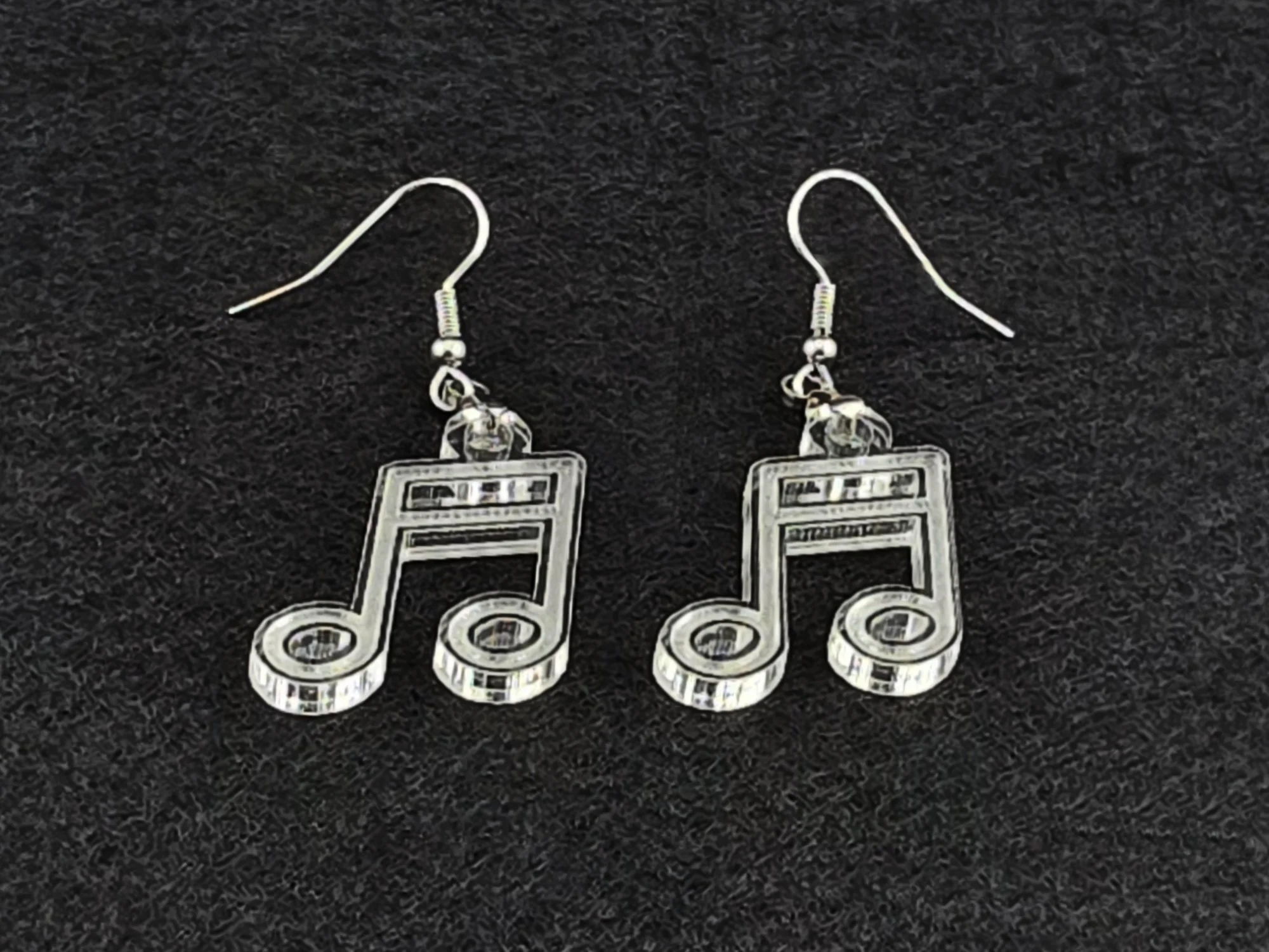 Pair of clear acrylic beam note earrings shown at an angle on a charcoal background, highlighting the cut linework with no color tint.