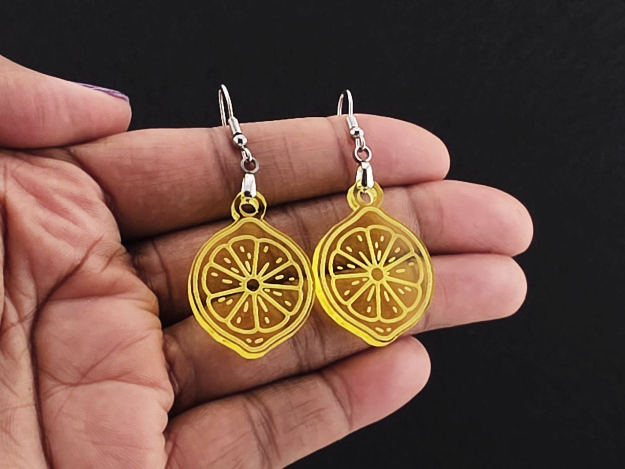 Lemon slice earrings resting in an open palm on a charcoal background, shown for scale.
