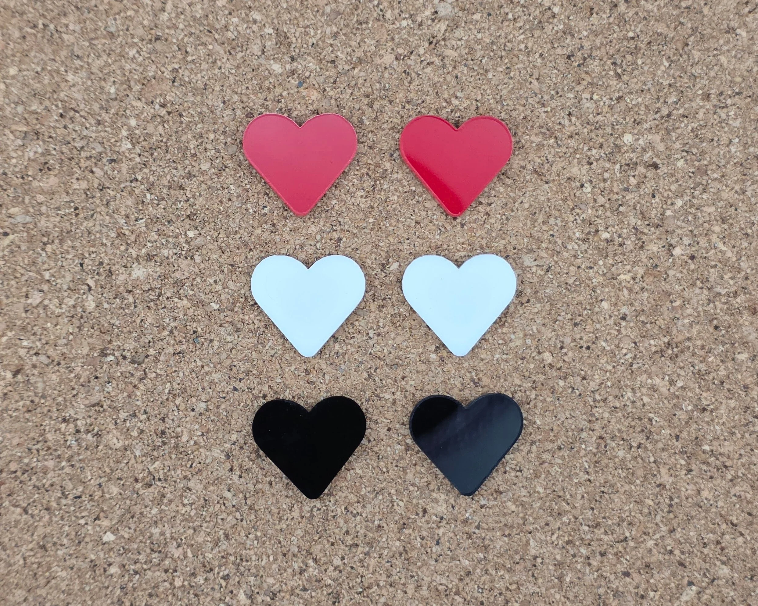 Red, white, and black acrylic heart stud earrings displayed on cork board, handmade colorful heart studs with hypoallergenic titanium posts by Rainbow Charlie