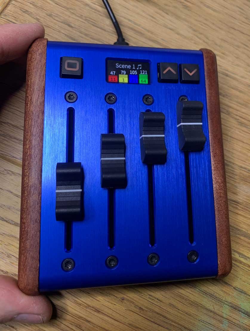 Top view of a tiny programmable MIDI fader with blue aluminum top and LCD screen