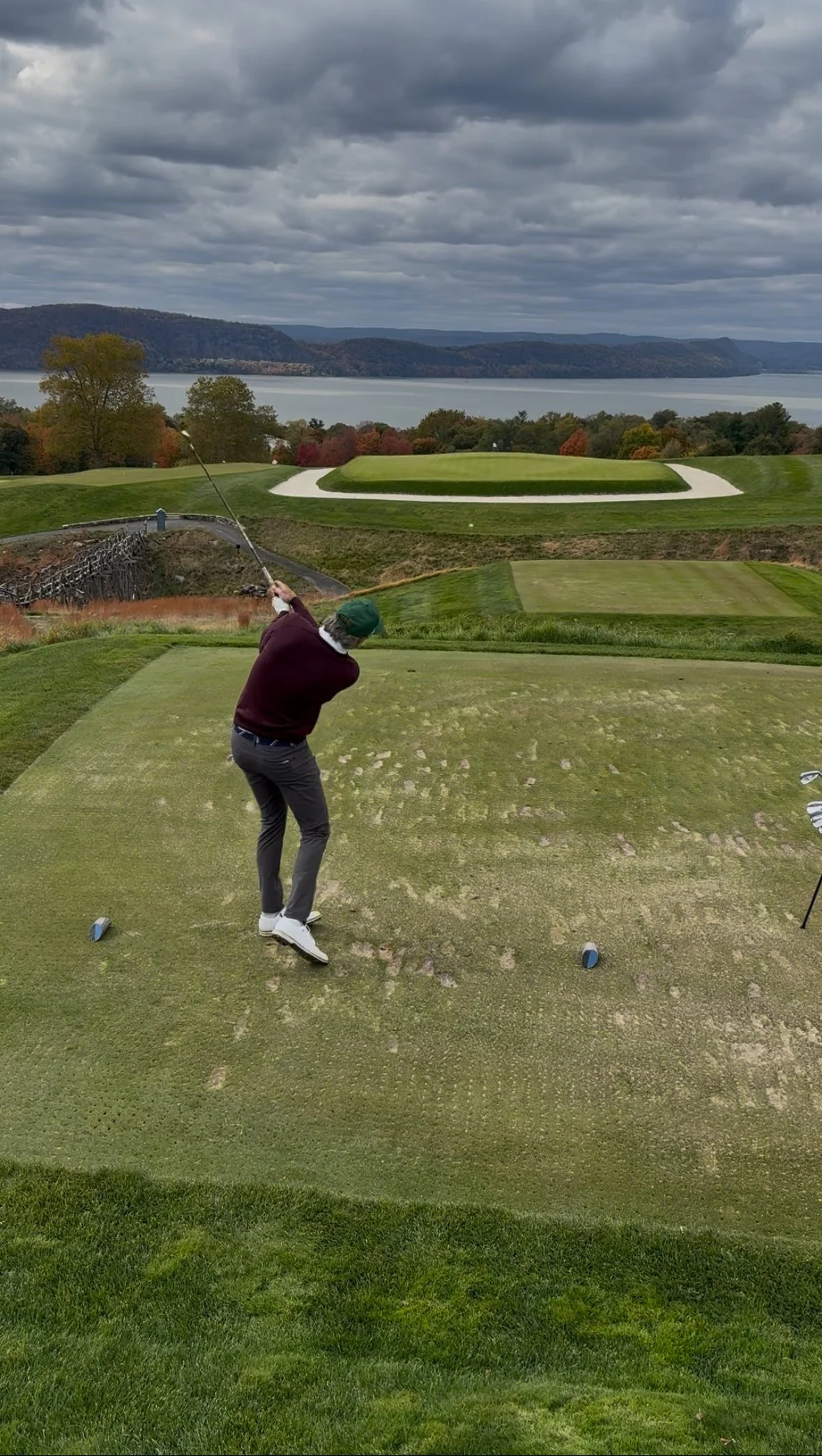 A man hitting a golf ball to a hole overlooking the Hudson River.