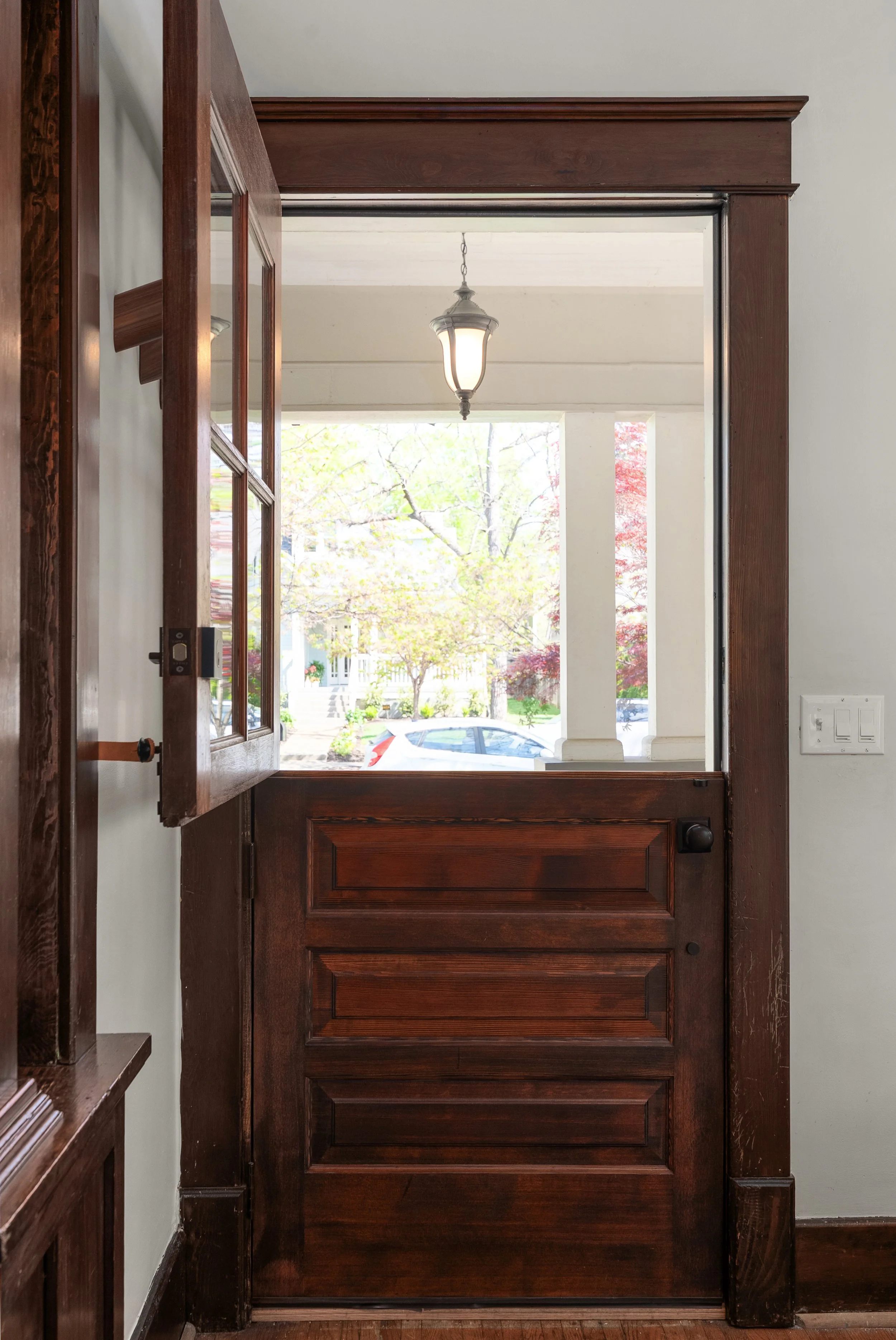 View through glass doors showing a pathway lined with small trees leading to an open backyard with a clear sky.