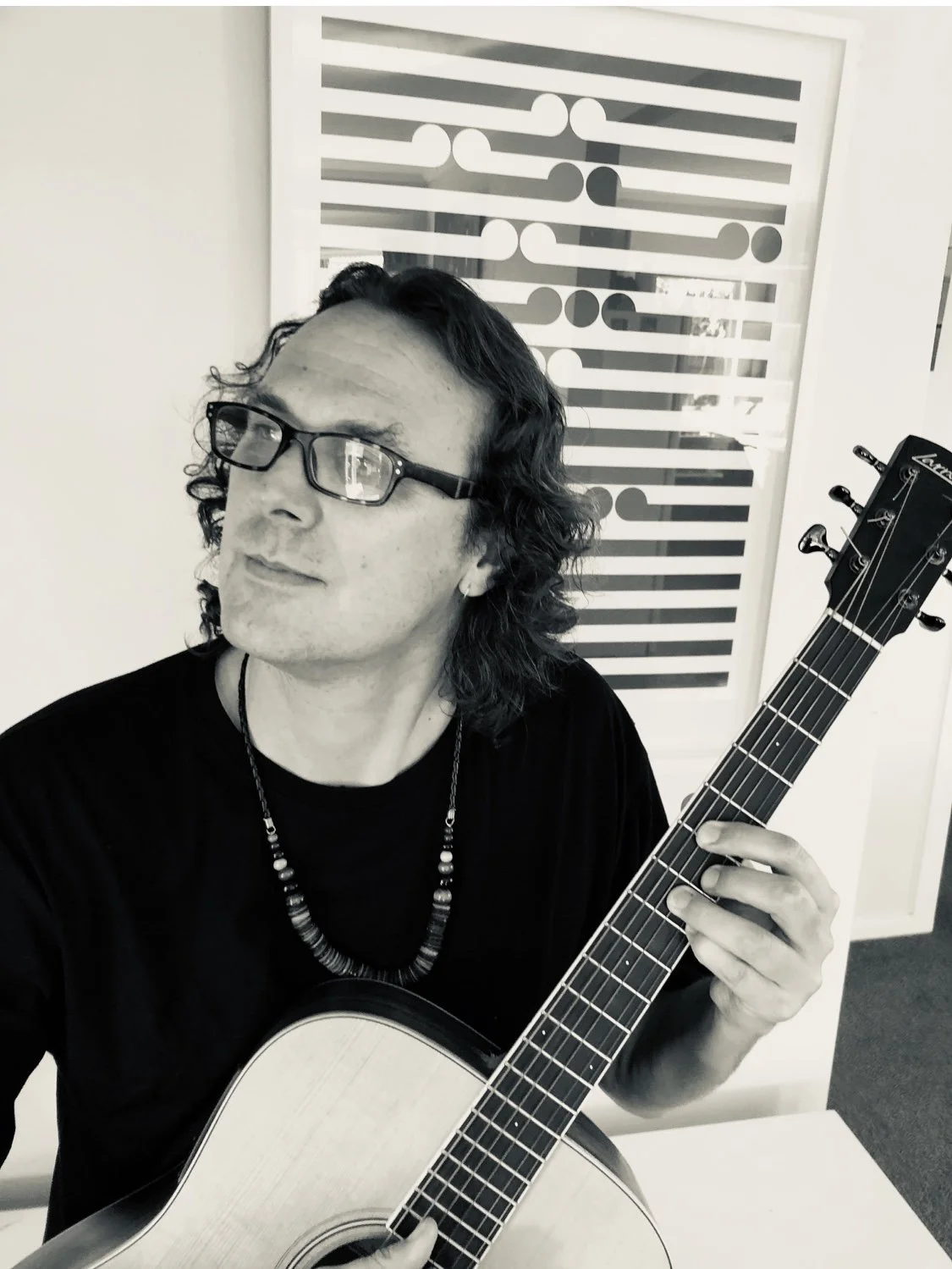 Person playing an acoustic guitar indoors with abstract art on the wall.