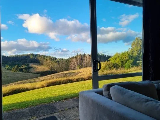 View of grassy hills and trees through a large window, with a couch indoors in the foreground in the designated therapy room. at Keystone Lodge