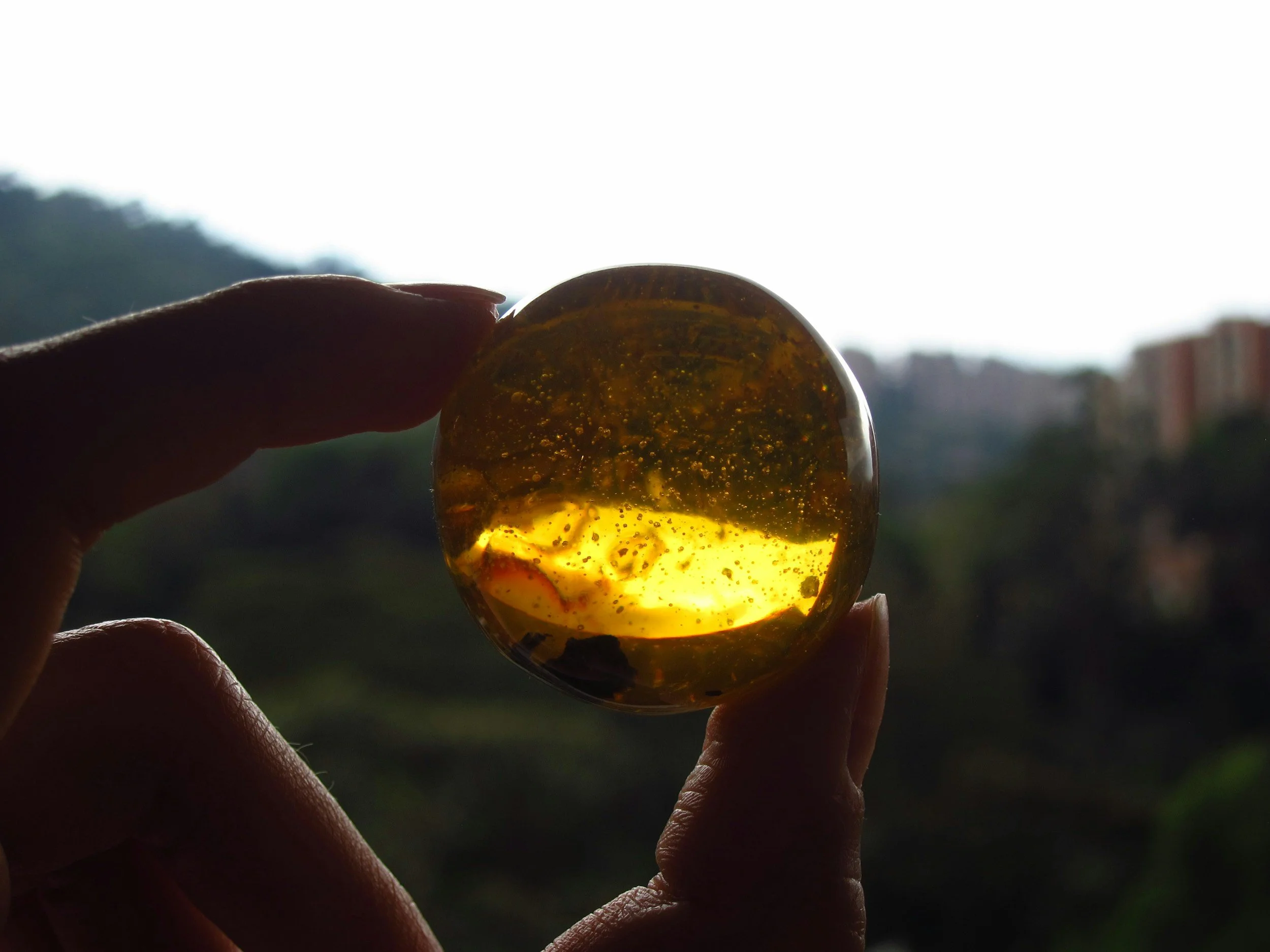 Hand holding a translucent amber gemstone against a bright sky background.