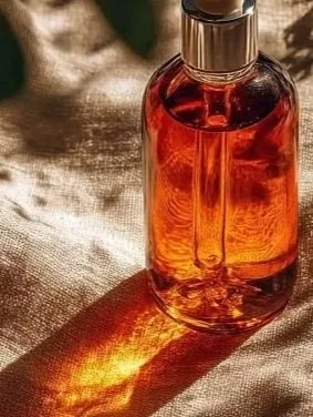 A glass perfume bottle filled with amber-colored liquid on a reflective surface with warm lighting.