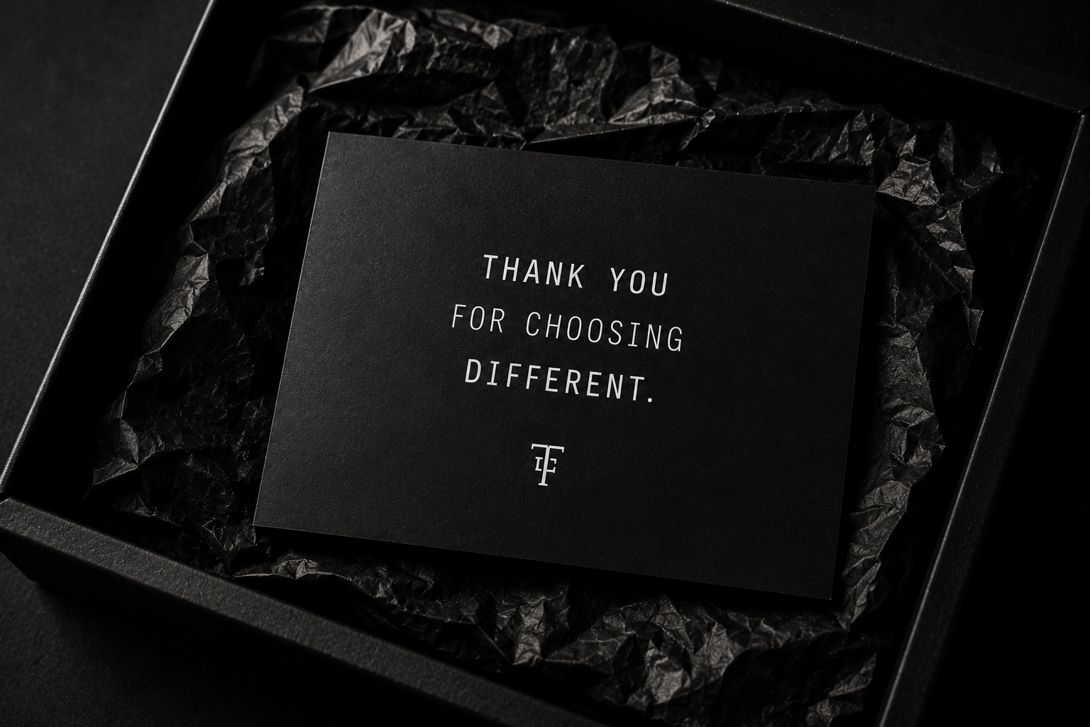 A black gift box containing black tissue paper and a black card that says, "Thank you for choosing different" with a small logo at the bottom.