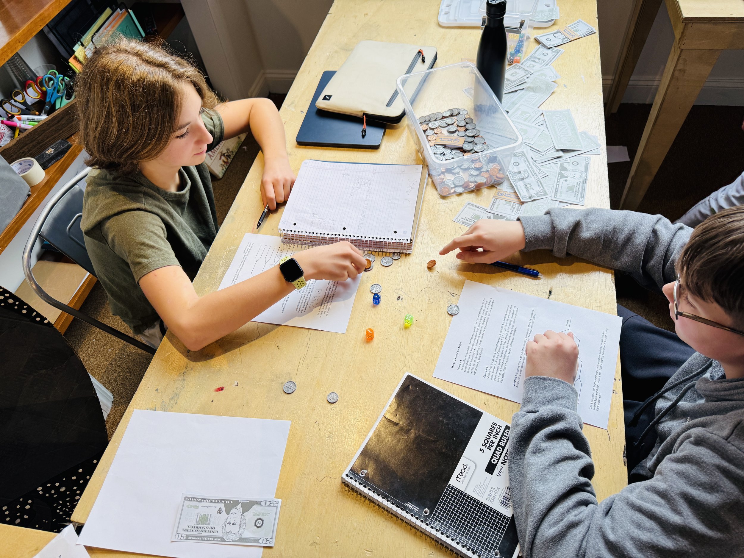 Group of graduates in black caps and gowns with orange stoles taking a selfie with a man in glasses and a woman in a blue dress in a hallway.
