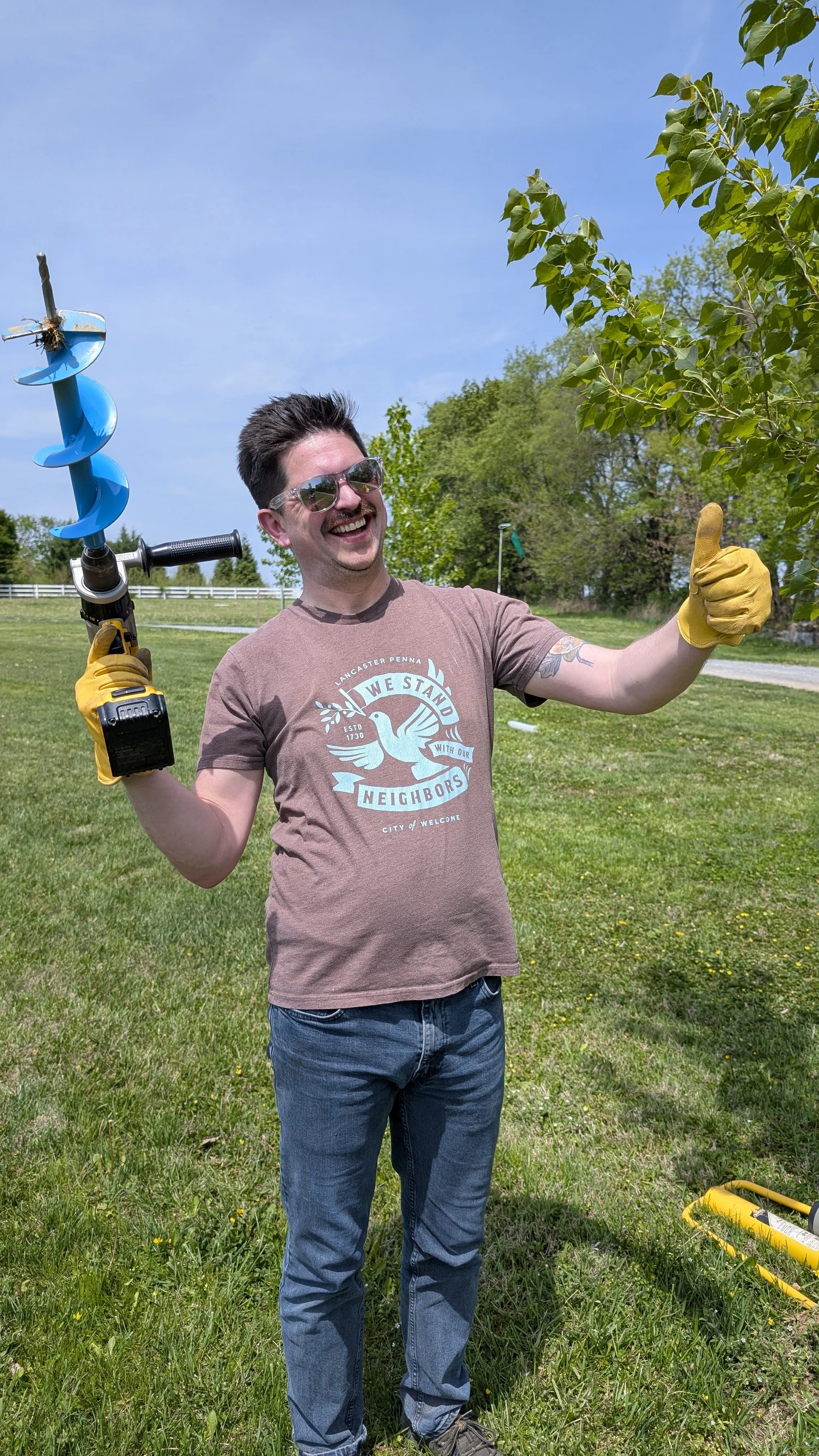 A woman and a man standing outdoors in a parking lot, each wearing a blue inflatable swim ring around their waist. The woman is smiling, wearing sunglasses, a white shirt, and a scarf. The man has a gray beard, glasses, and is wearing a black Patagonia hoodie. They are posing with their arms around each other.