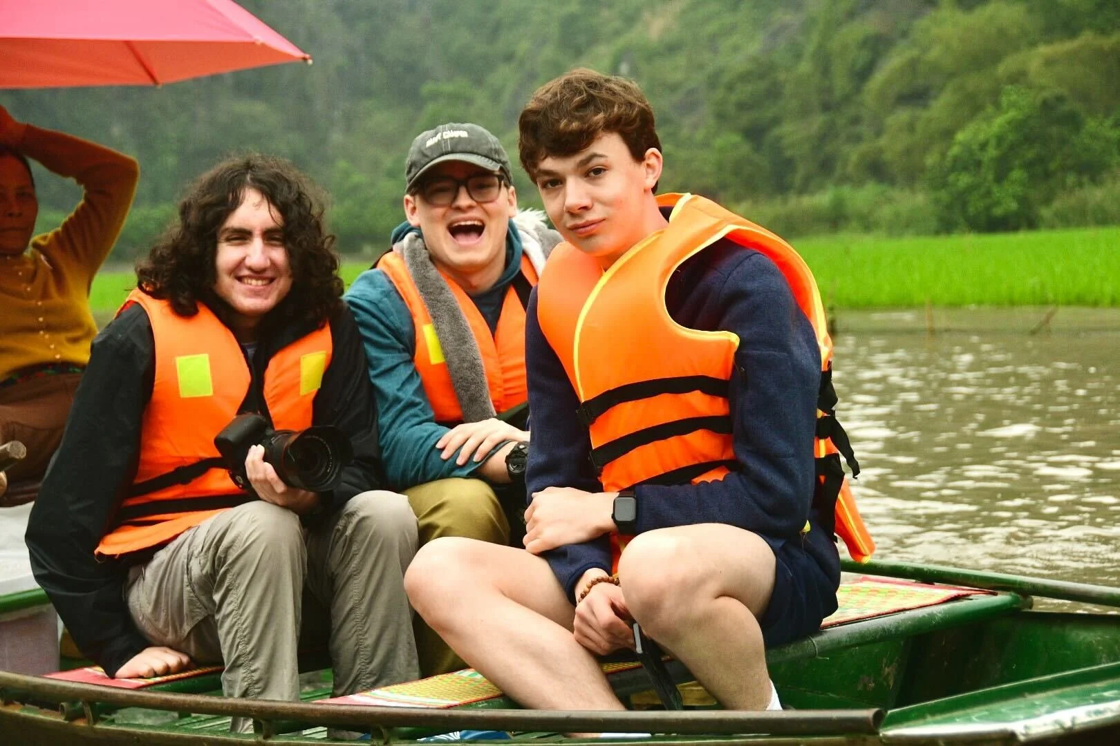 A woman speaking at a podium in front of a seated audience in a well-lit room decorated with artwork and greenery.