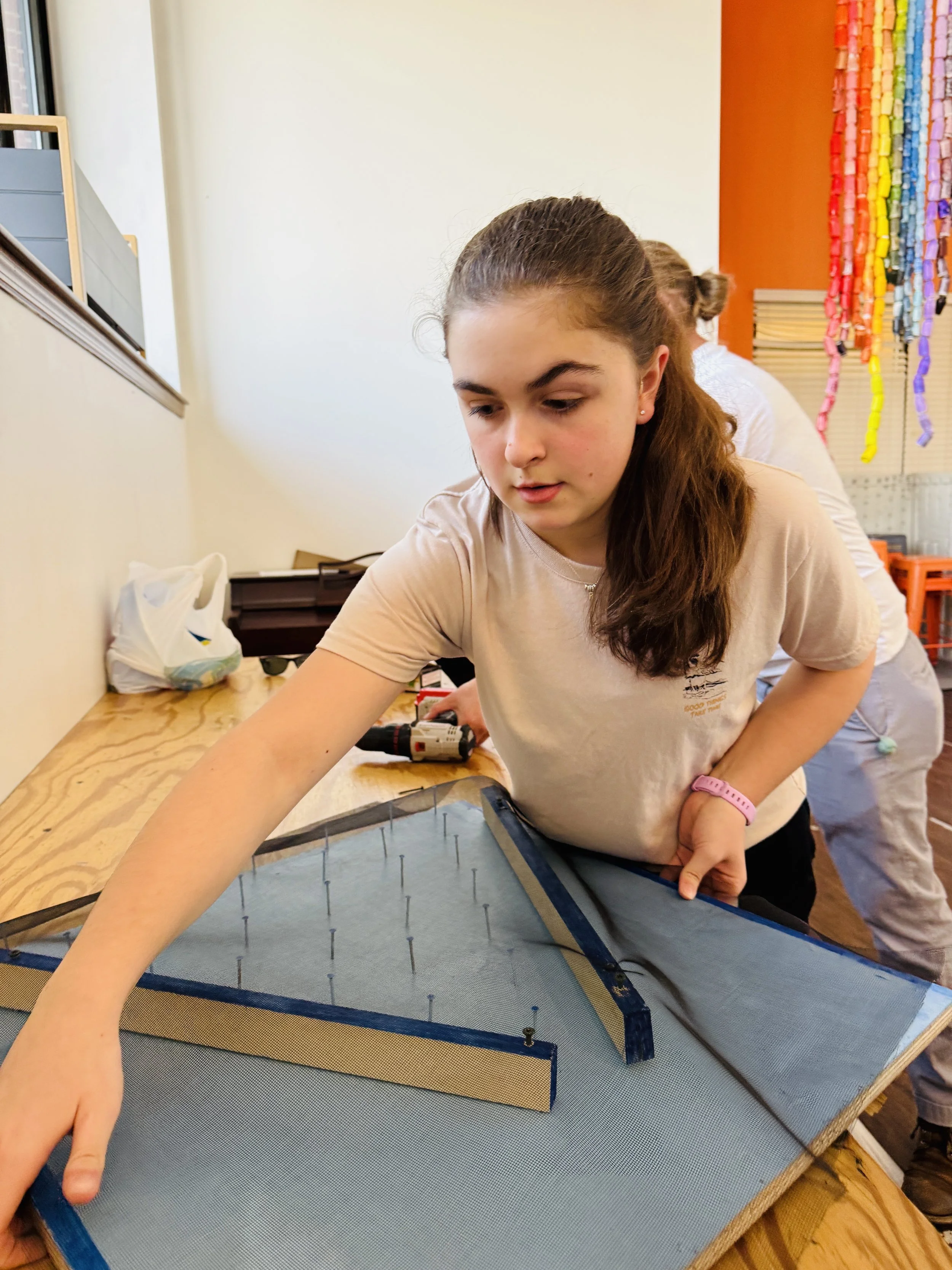 Three women and a man, wearing a chef's hat, sit at a kitchen counter with pizza in front of them, smiling and having a conversation.