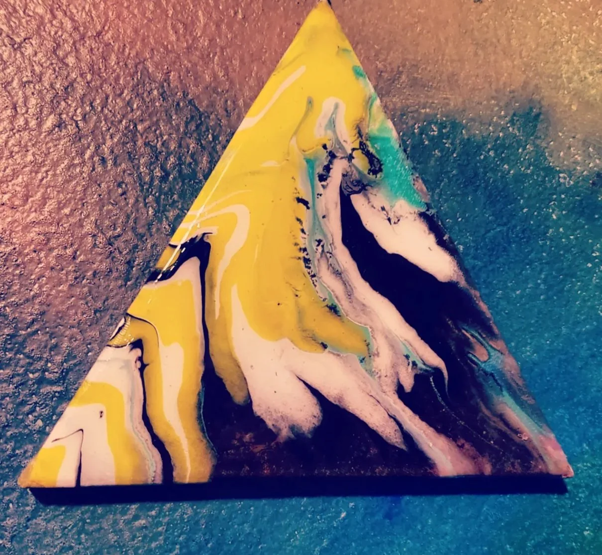 A colorful, abstract, triangular-shaped object with swirling yellow, black, white, and green patterns resting on a textured surface.