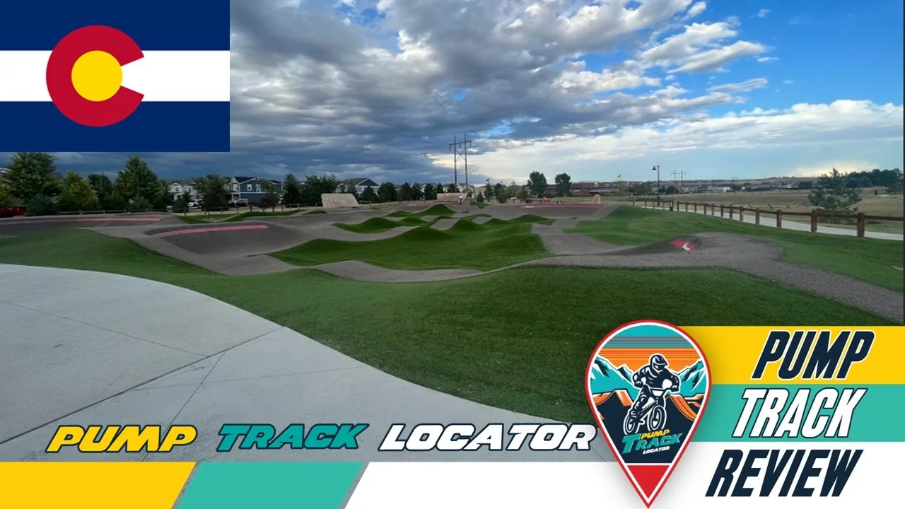 Image of a BMX pump track with a logo in the lower right corner and the Colorado state flag in the upper left corner. The scene shows a winding dirt track with green grass and overcast sky.