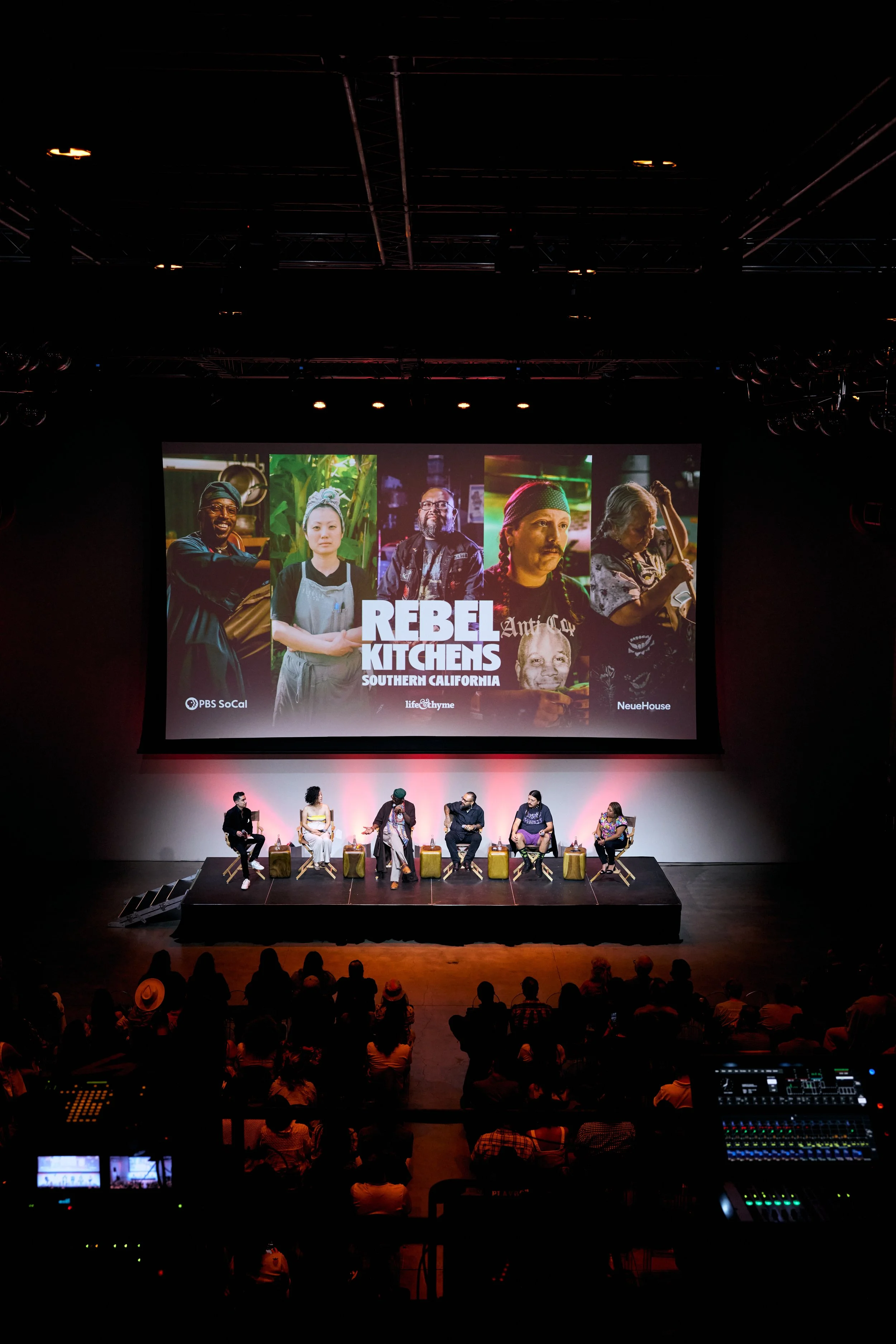 Panel discussion on stage with six people sitting in chairs, large screen behind them displays photos of diverse individuals and the text 'Rebel Kitchens Southern California,' with logos of PBS SoCal, life&thyme, and NeueHouse.