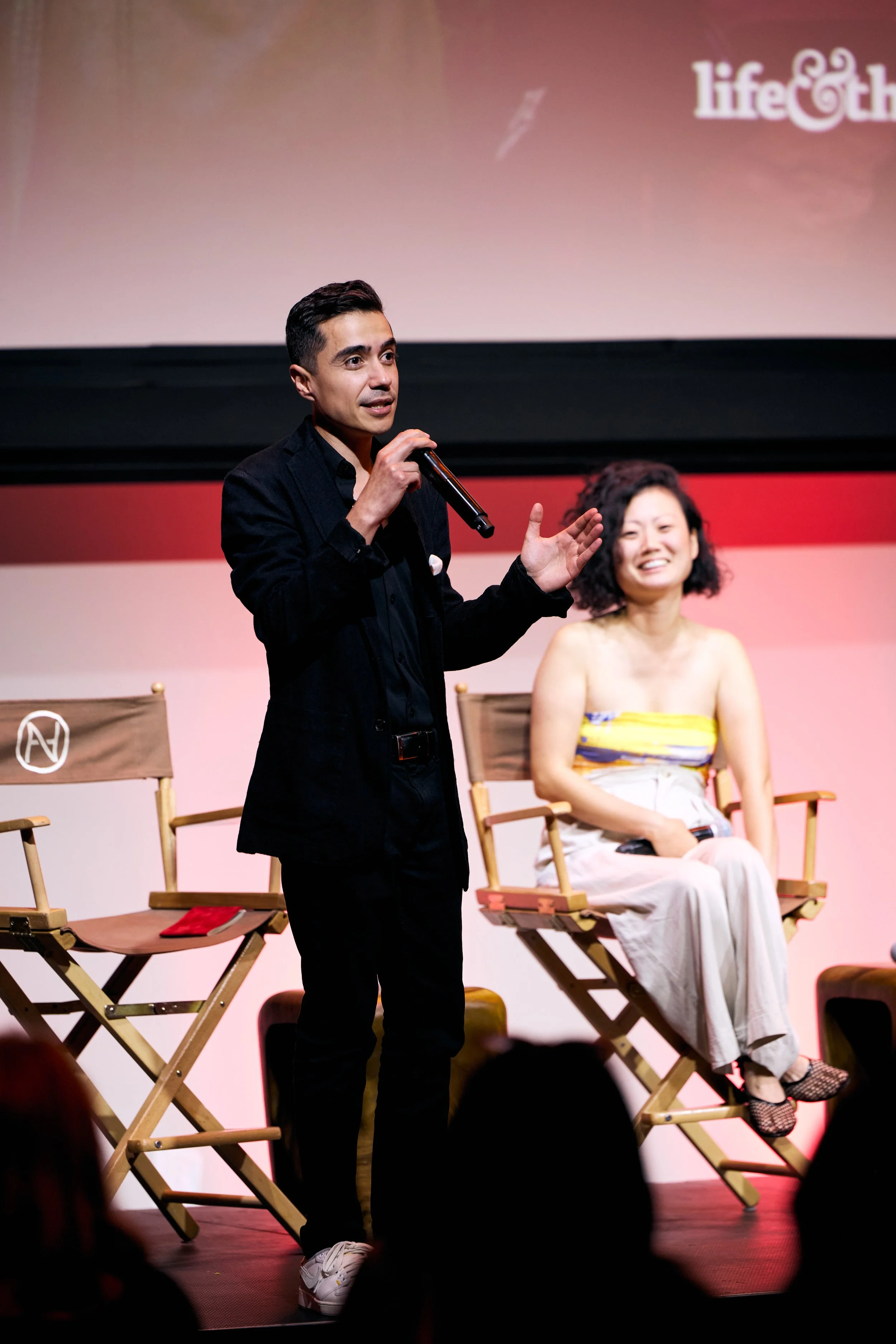 Antonio in a black suit speaking into a microphone on stage.