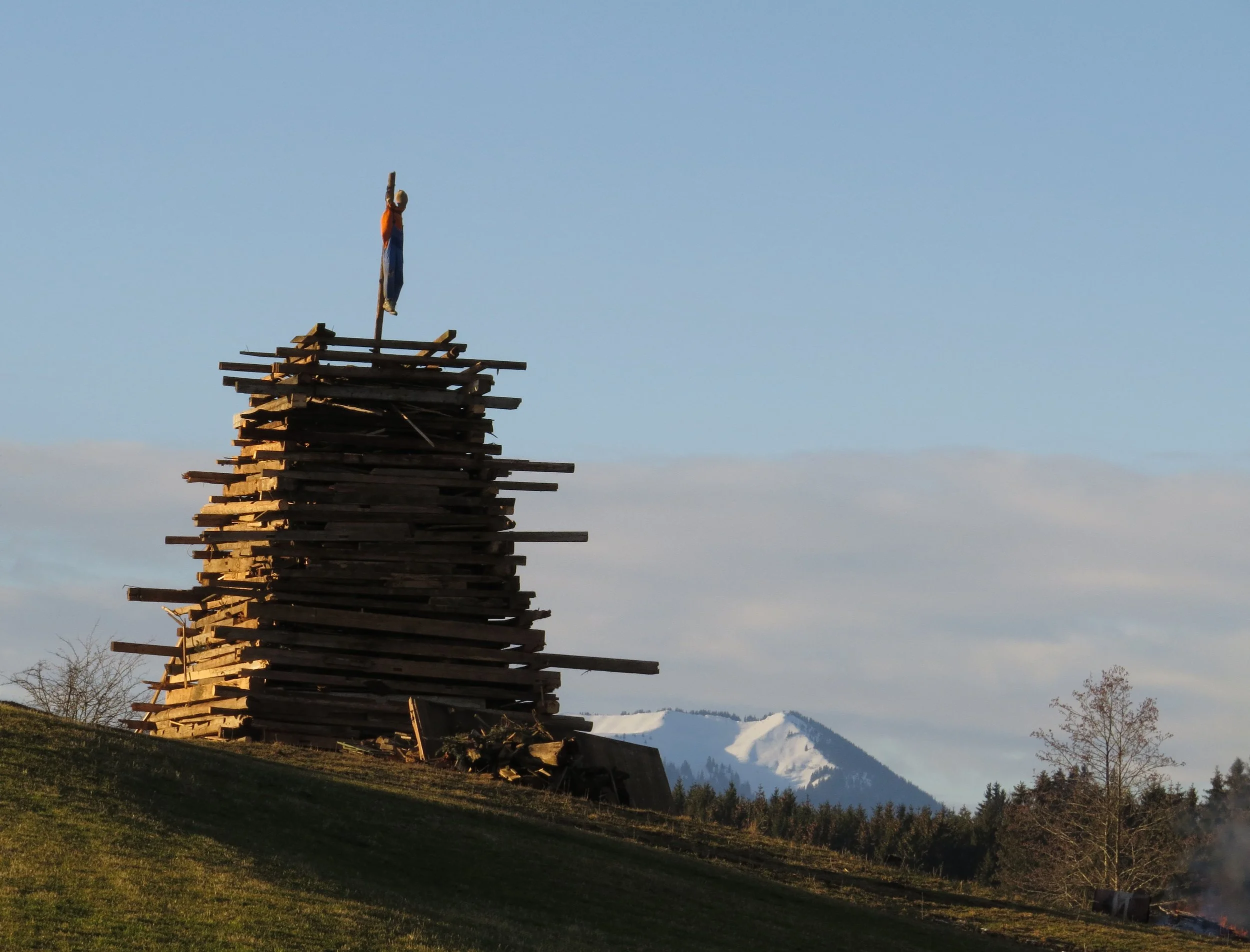 Holzstapel mit Strohpuppe vor Bergen