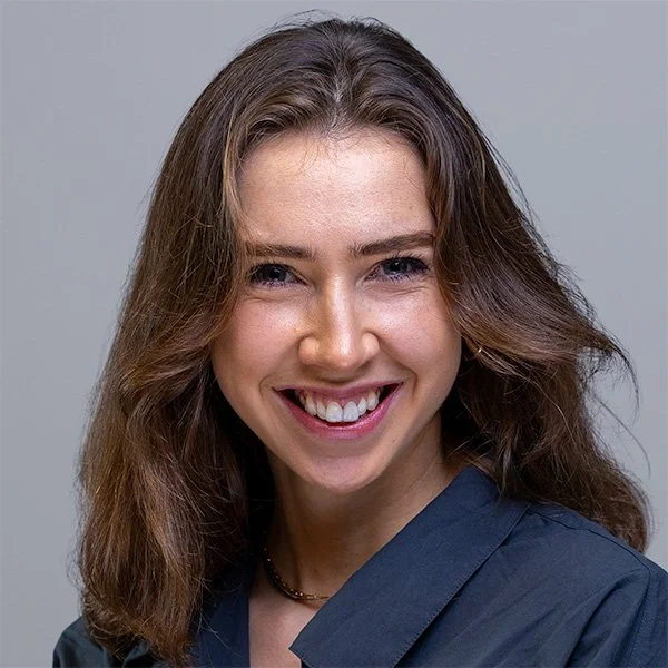 Young woman with dark wavy hair in a navy blazer, confident warm smile — LinkedIn profile photo London | Shot By Andrew