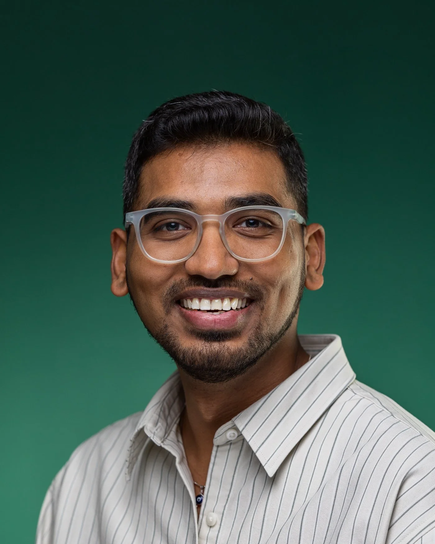Corporate headshot of a smiling man in glasses and a cream striped shirt on a deep green background | Corporate headshots Vauxhall, London | Shot By Andrew