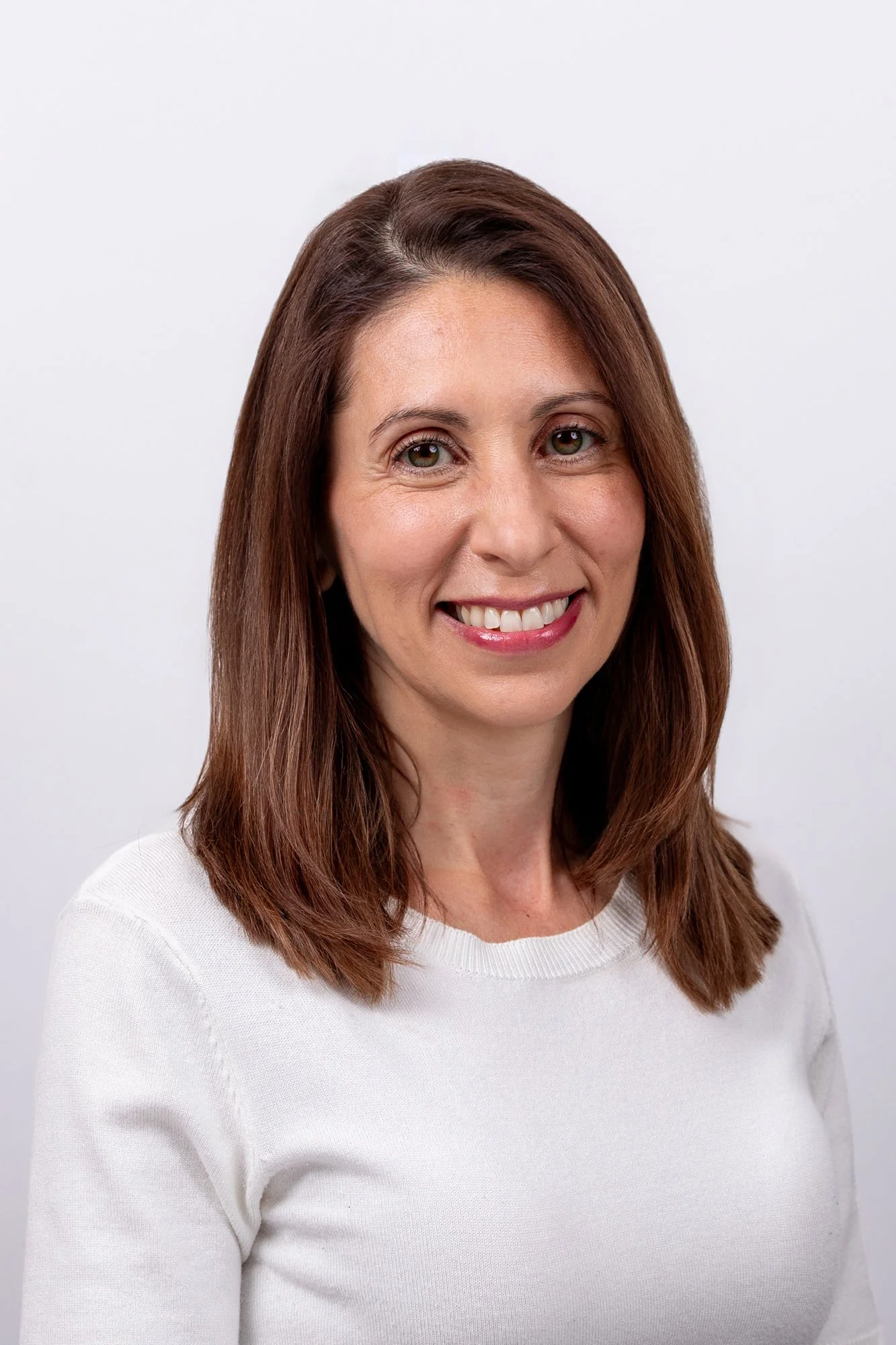 Corporate headshot of a smiling woman with auburn hair in a cream jumper, pale grey background | Corporate headshots Victoria, London | Shot By Andrew