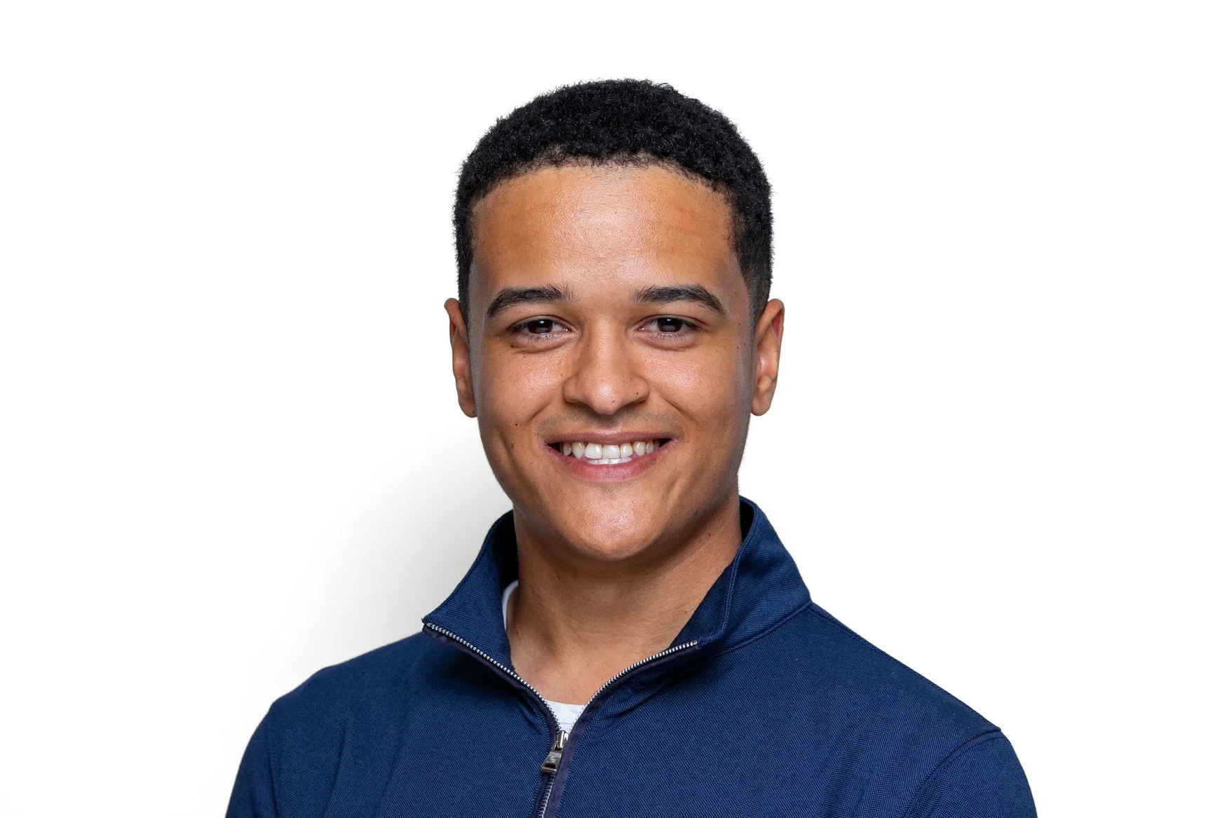 Smiling young man in a navy quarter-zip on a white background, a professional LinkedIn headshot taken in London