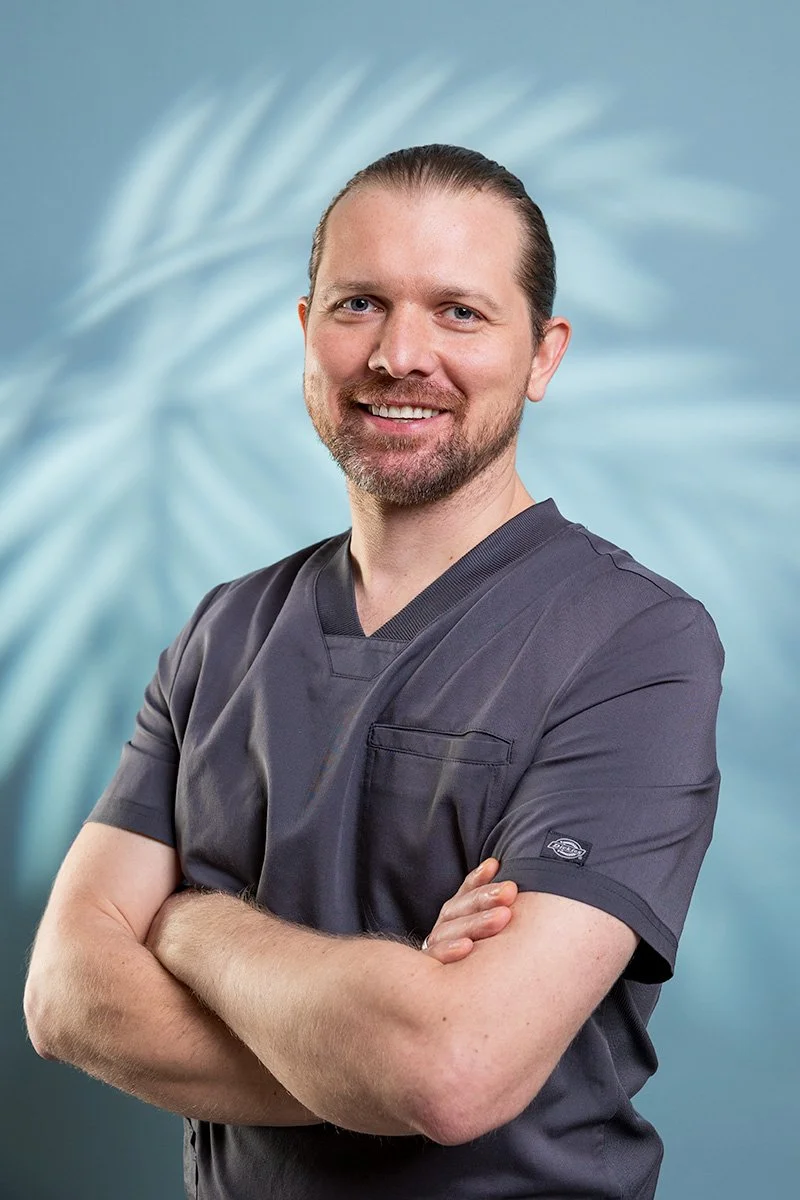 Man in dark grey scrubs with arms crossed and a warm smile — industry-appropriate clothing for professional LinkedIn photos London | Shot By Andrew