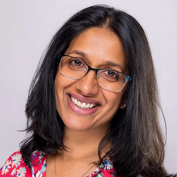 Woman with glasses and dark hair wearing a colourful top, wide bright smile — professional LinkedIn photos London | Shot By Andrew