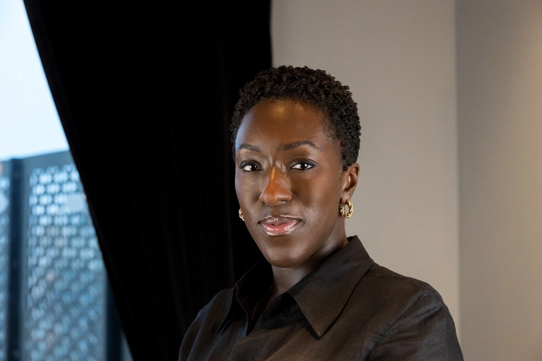 Corporate headshot of a woman with short cropped hair and gold earrings in a brown shirt, shot on location | London headshot photographer | Shot By Andrew